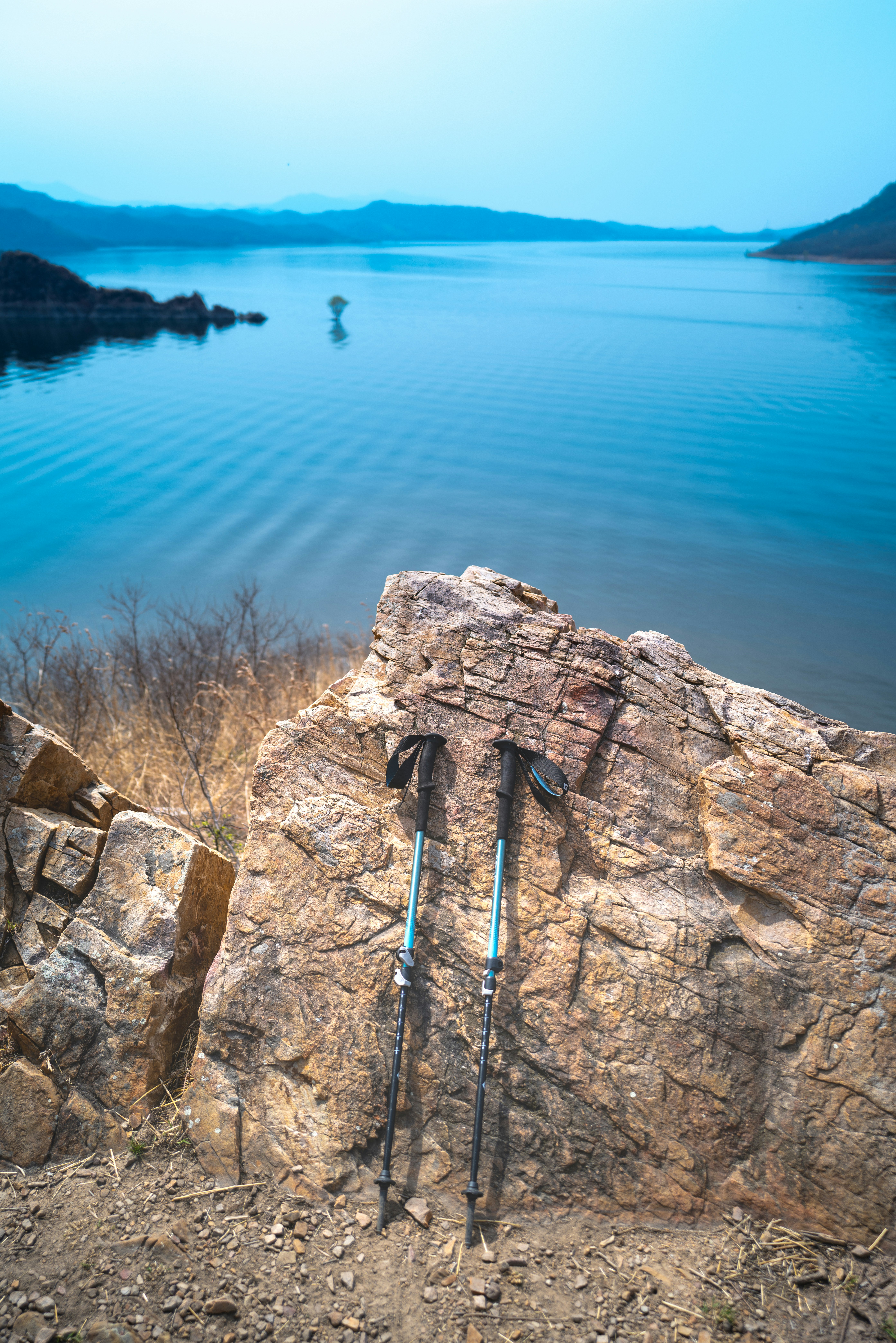 Bastones de trekking descansan sobre una roca con vistas a un lago sereno.