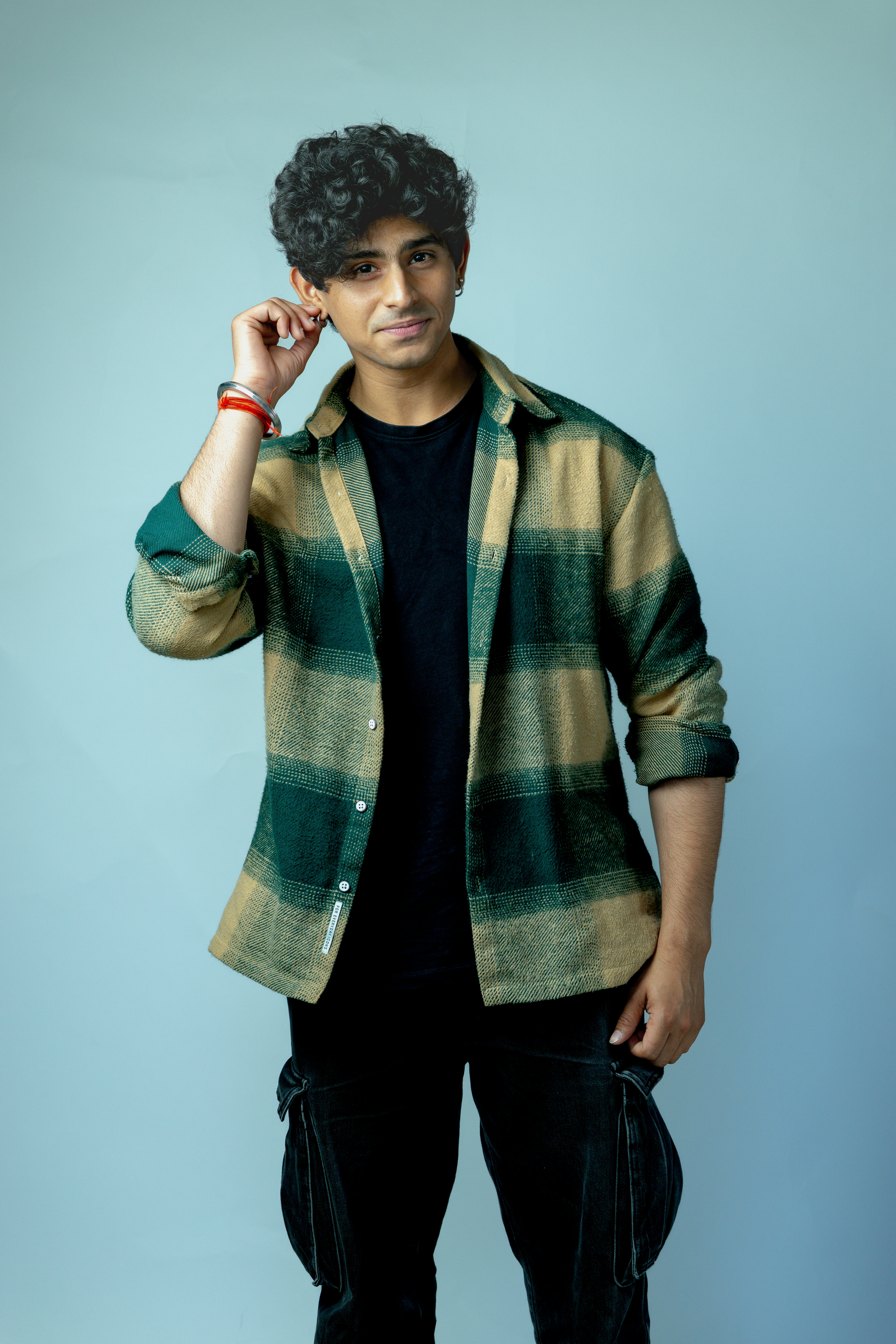 Man in plaid shirt adjusts earring against blue background