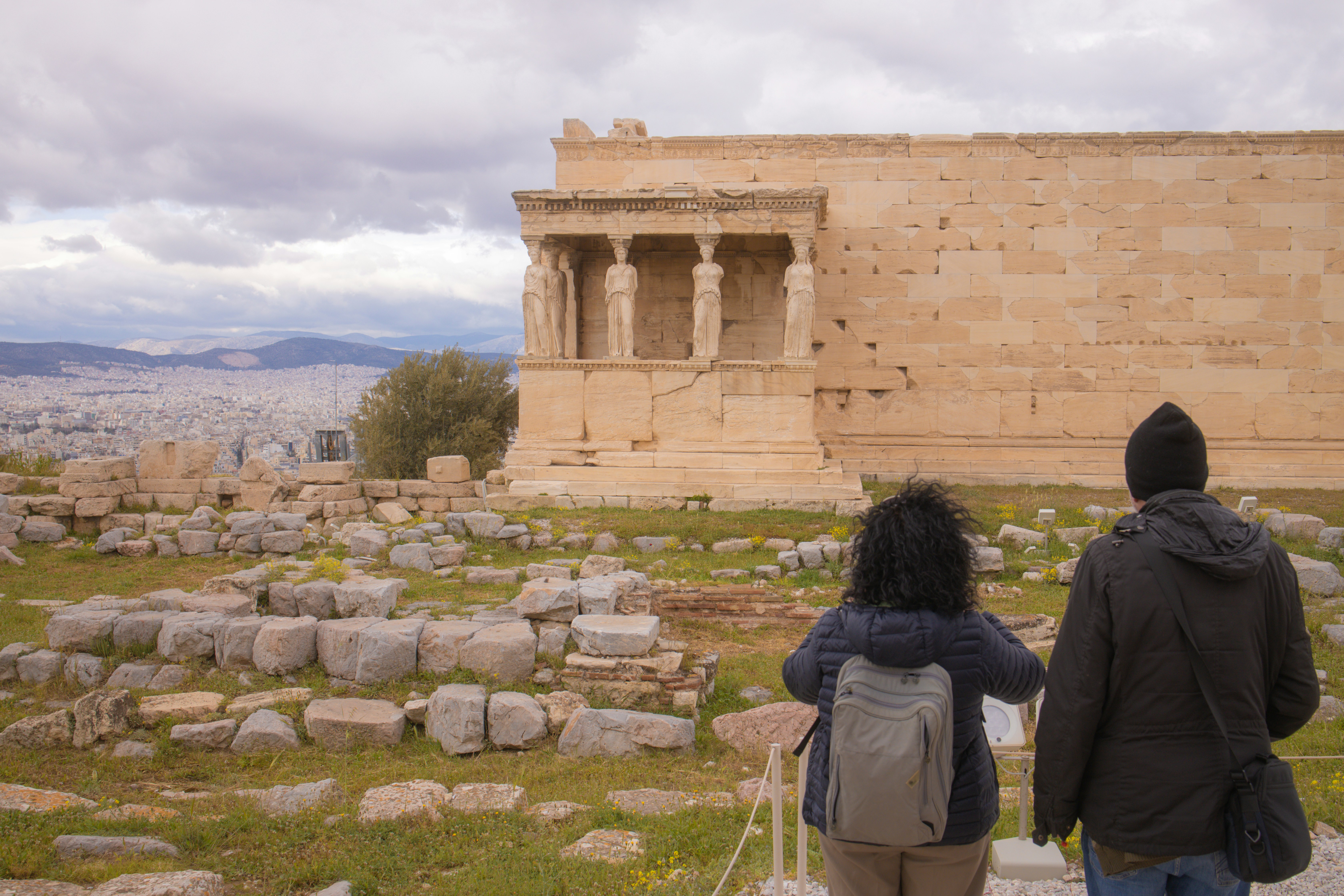 Two people view ancient ruins with city in background