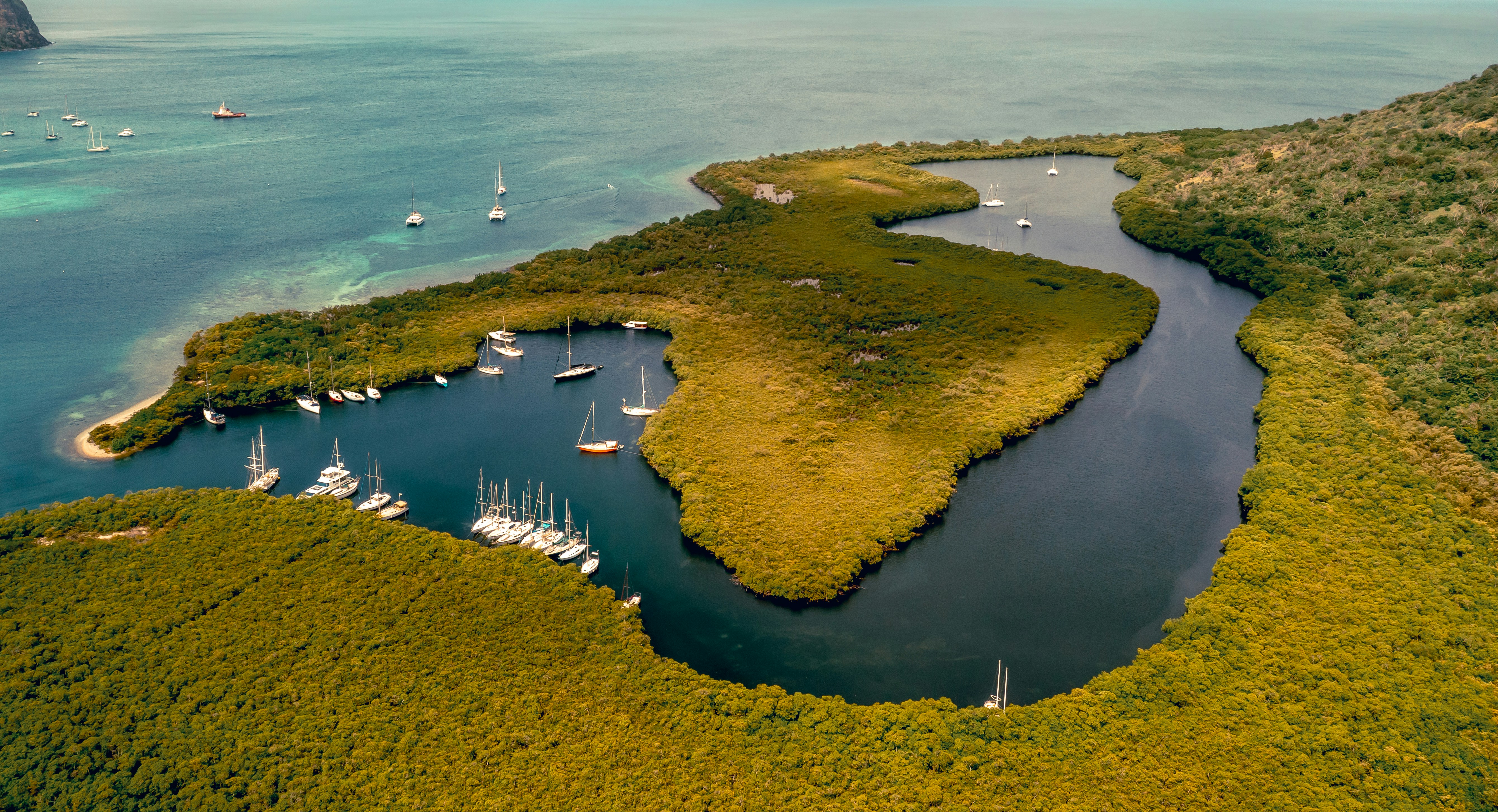 Sailboats anchored in a lush tropical bay.