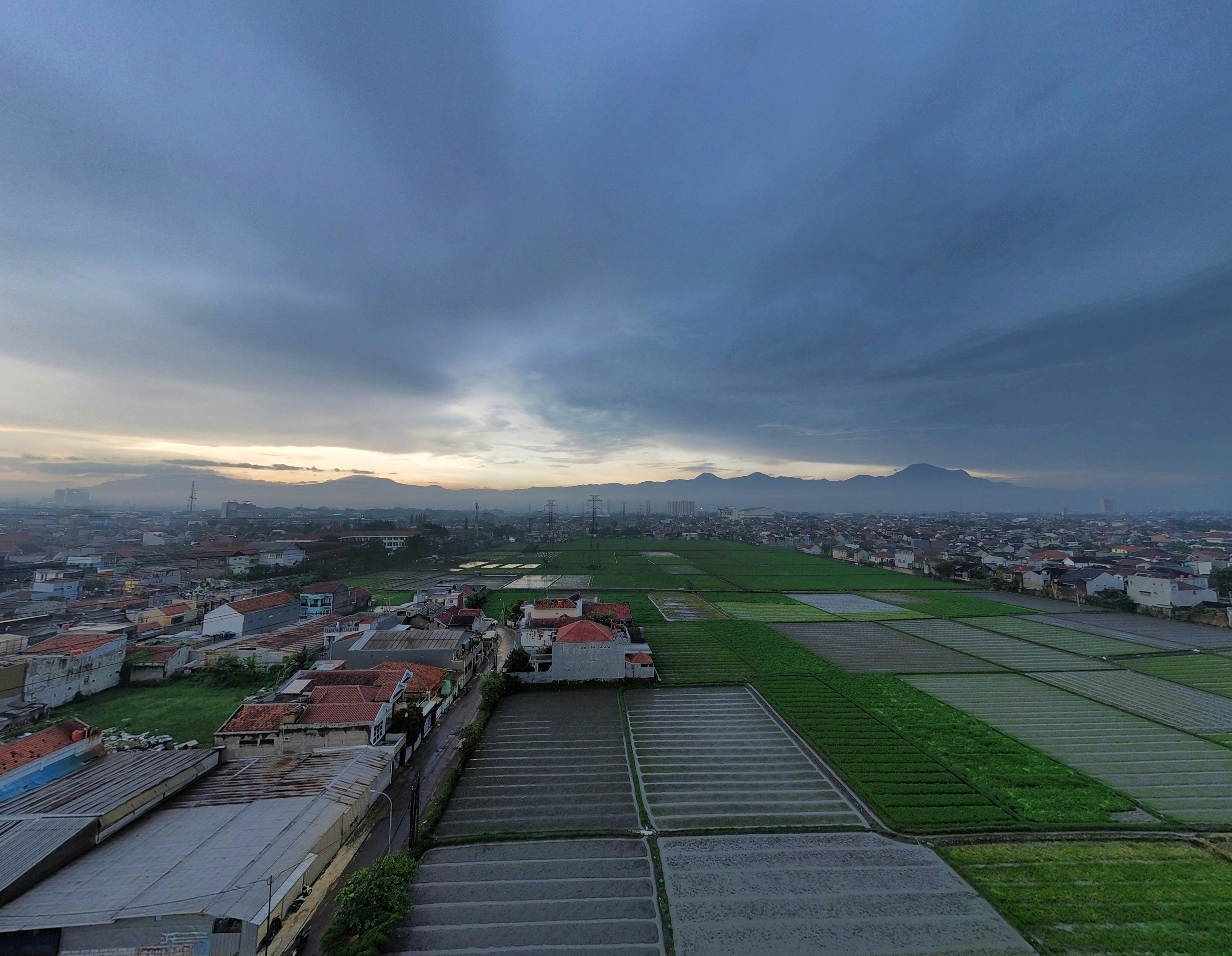Overcast sky above a rural town with rice fields.
