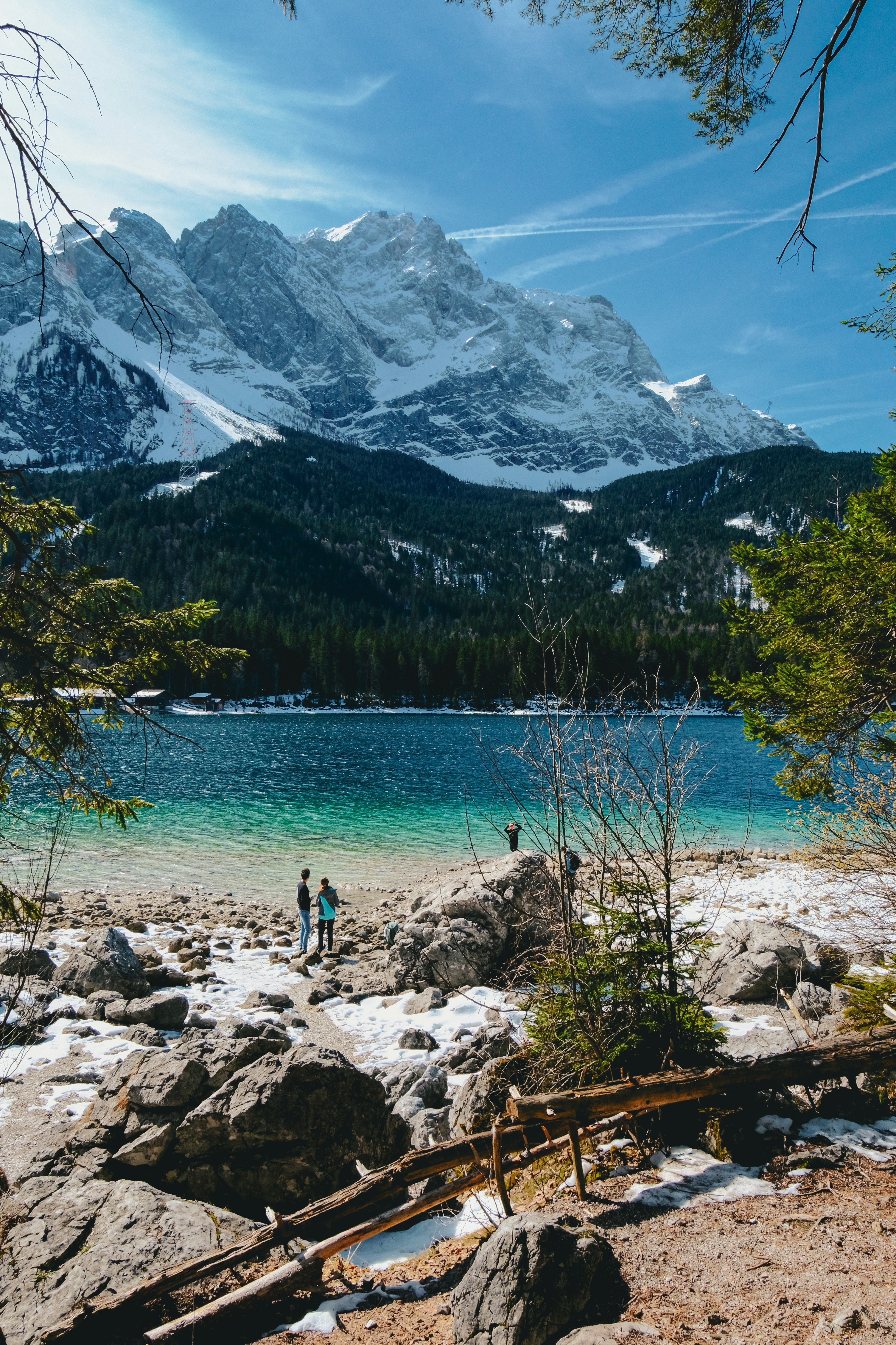 Des montagnes enneigées surplombent un lac turquoise avec des habitants sur le rivage.