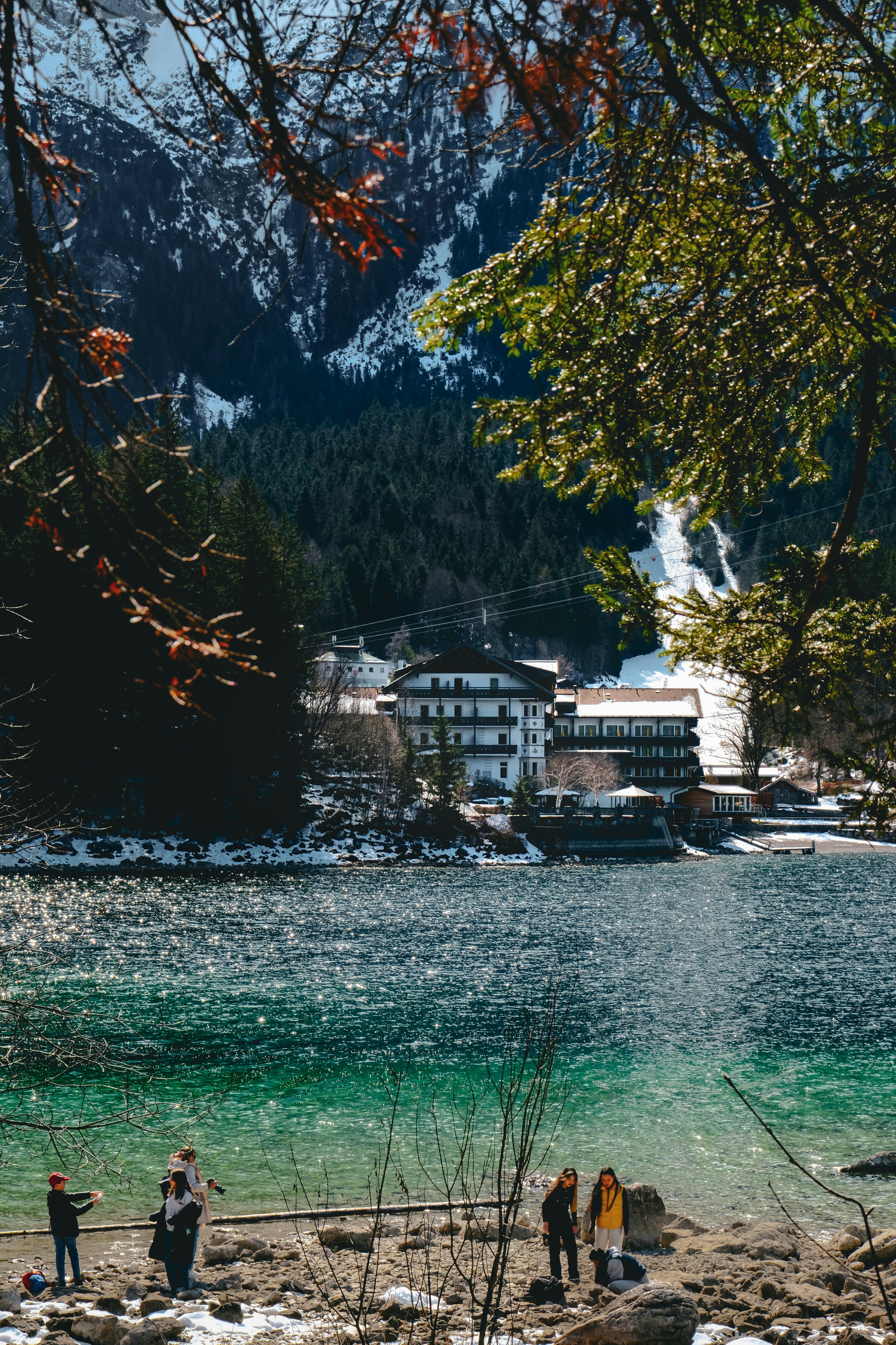 Des gens près d’un lac aux montagnes enneigées et aux bâtiments