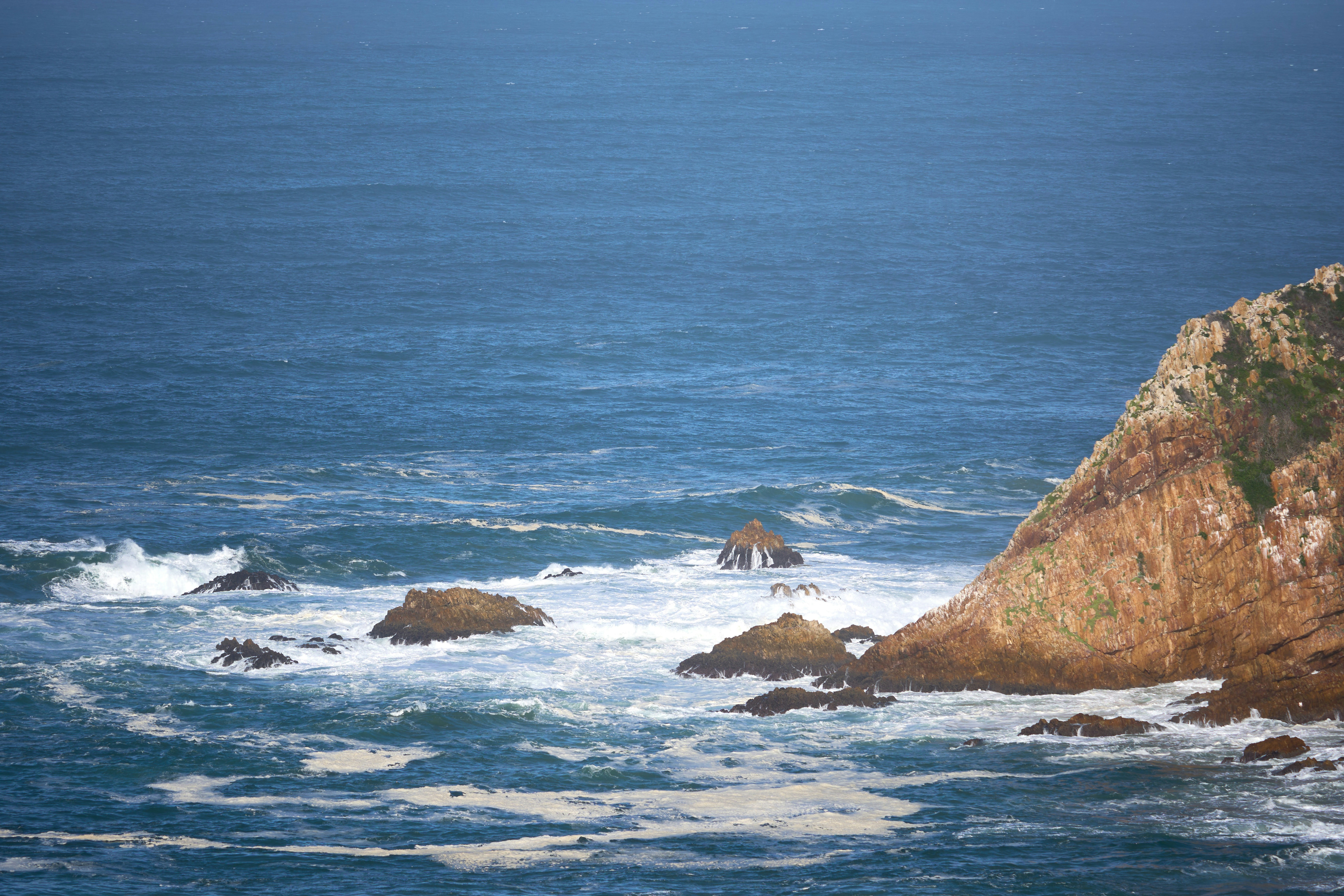 맑은 하늘 아래 바위 해안에 파도가 부딪힌다.