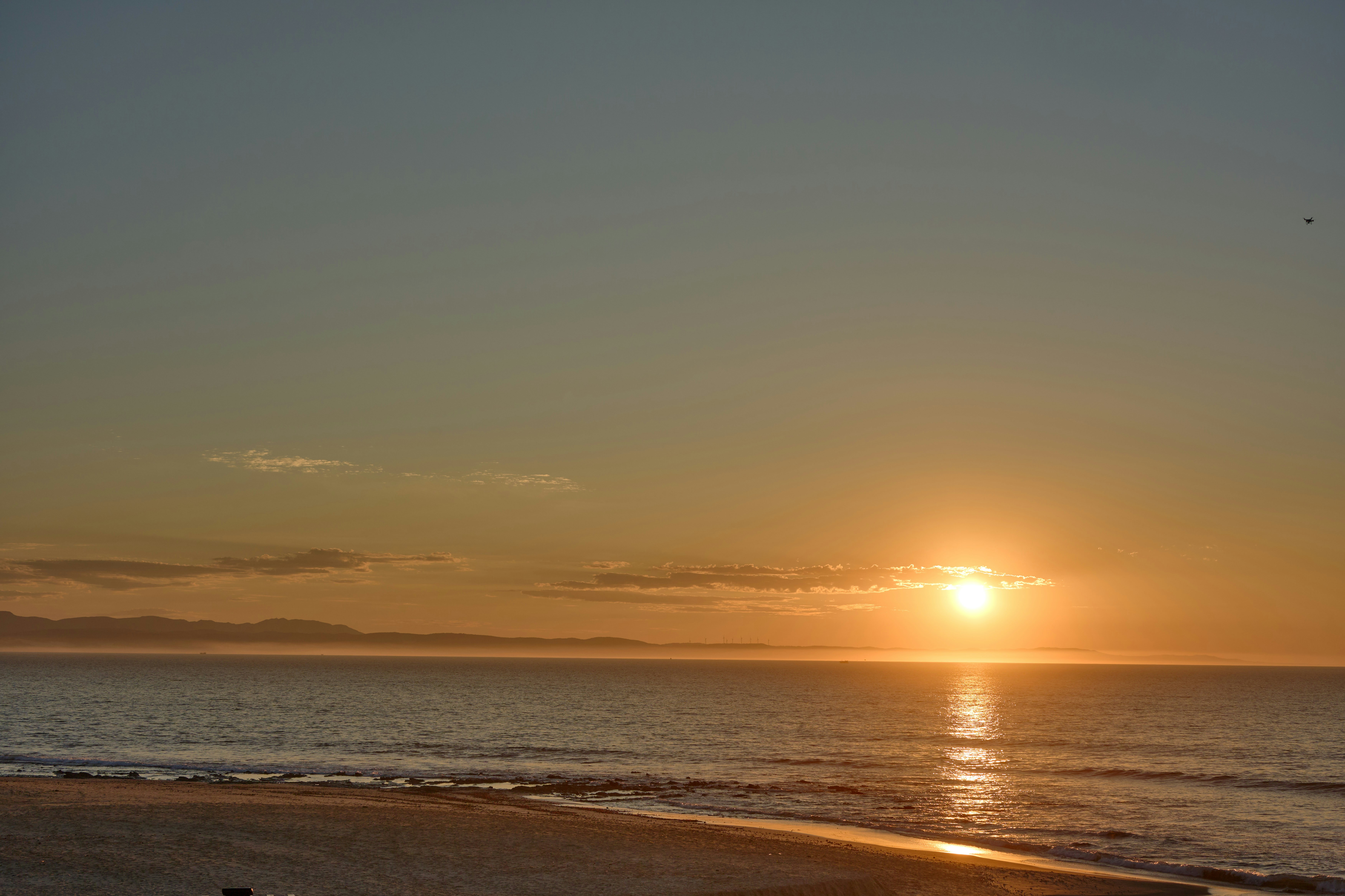 멀리 산들이 보이는 잔잔한 바다 위로 지는 일몰.