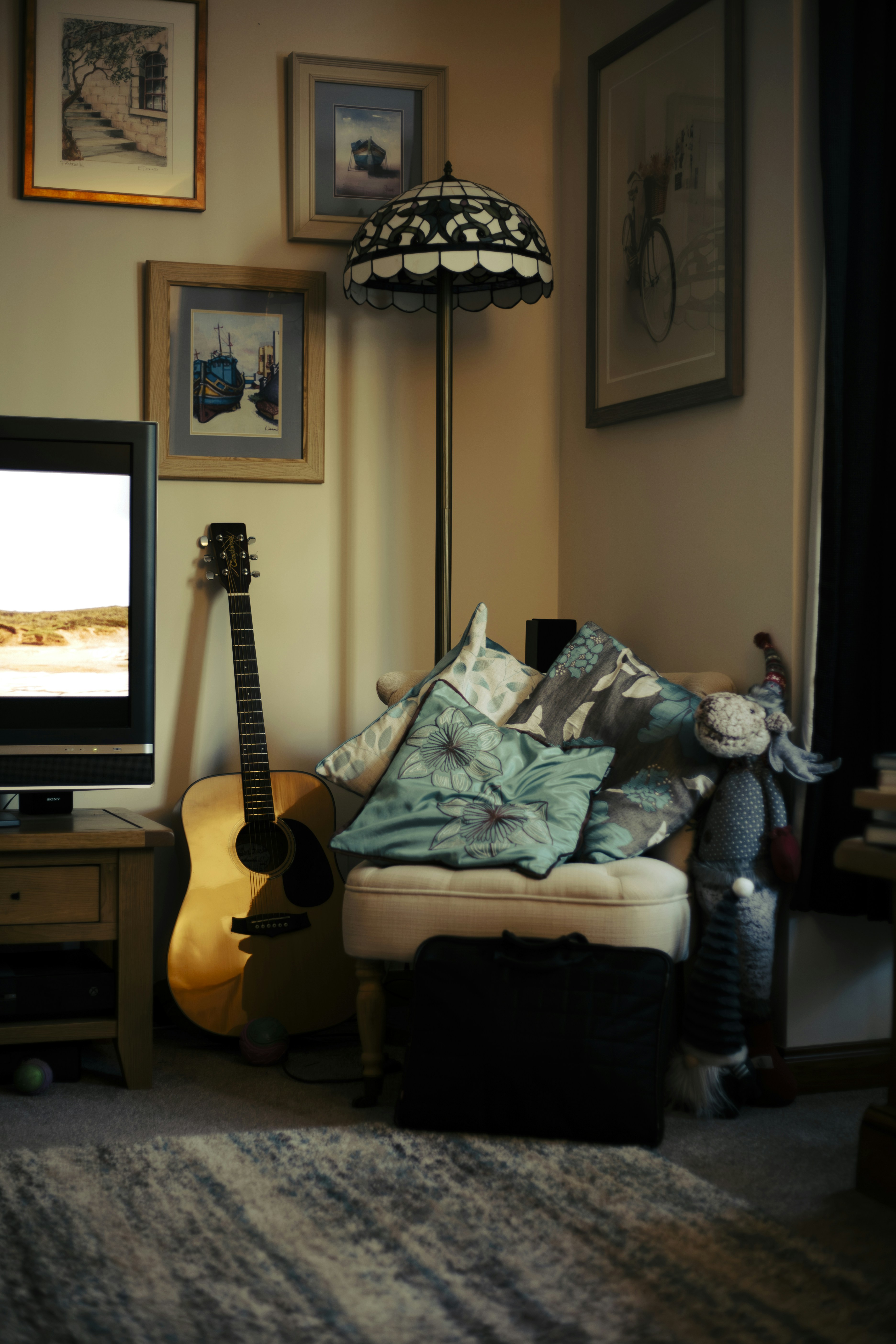 Acoustic guitar leaning against a chair with pillows.