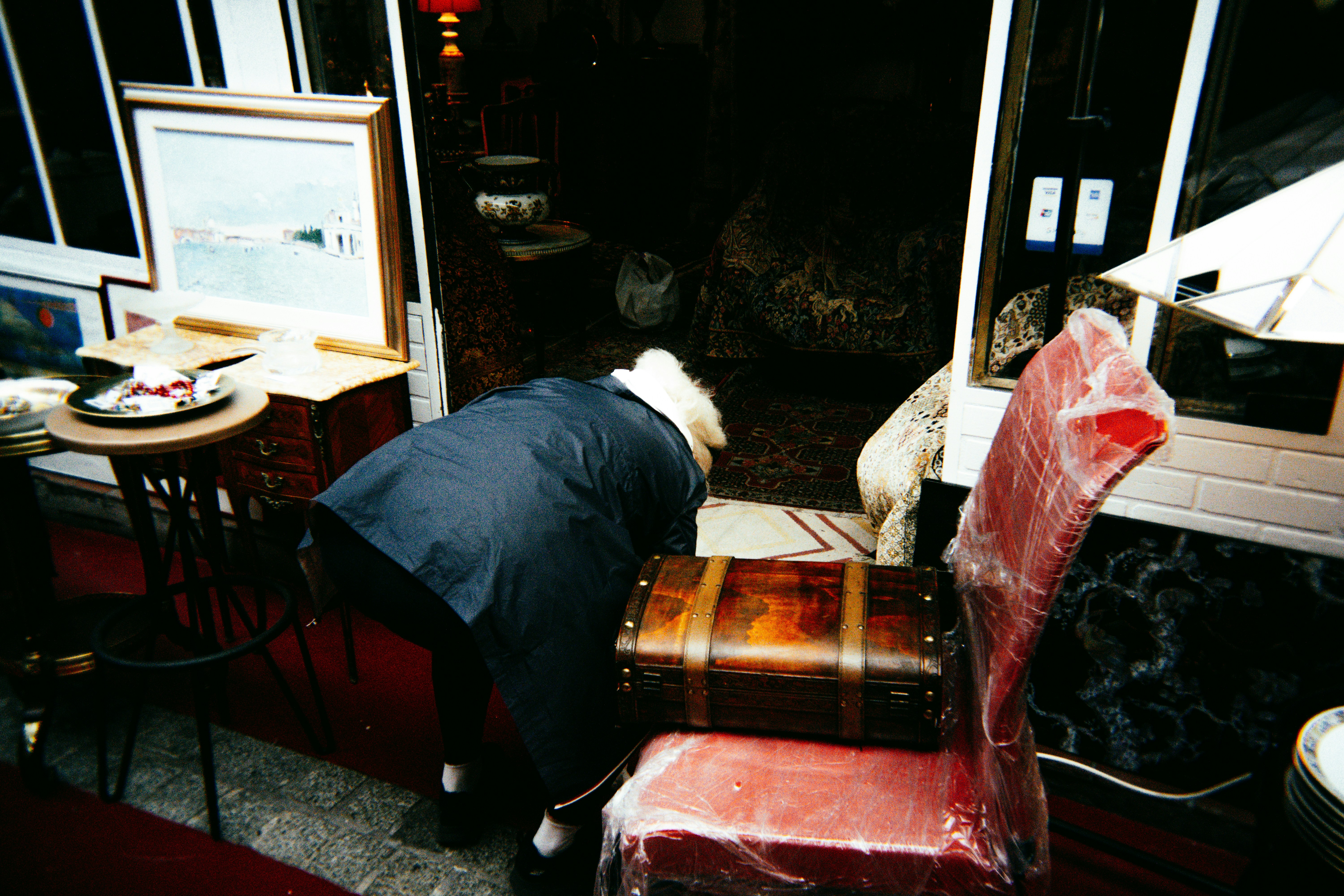 Person in suit bends over near vintage trunk and chair.