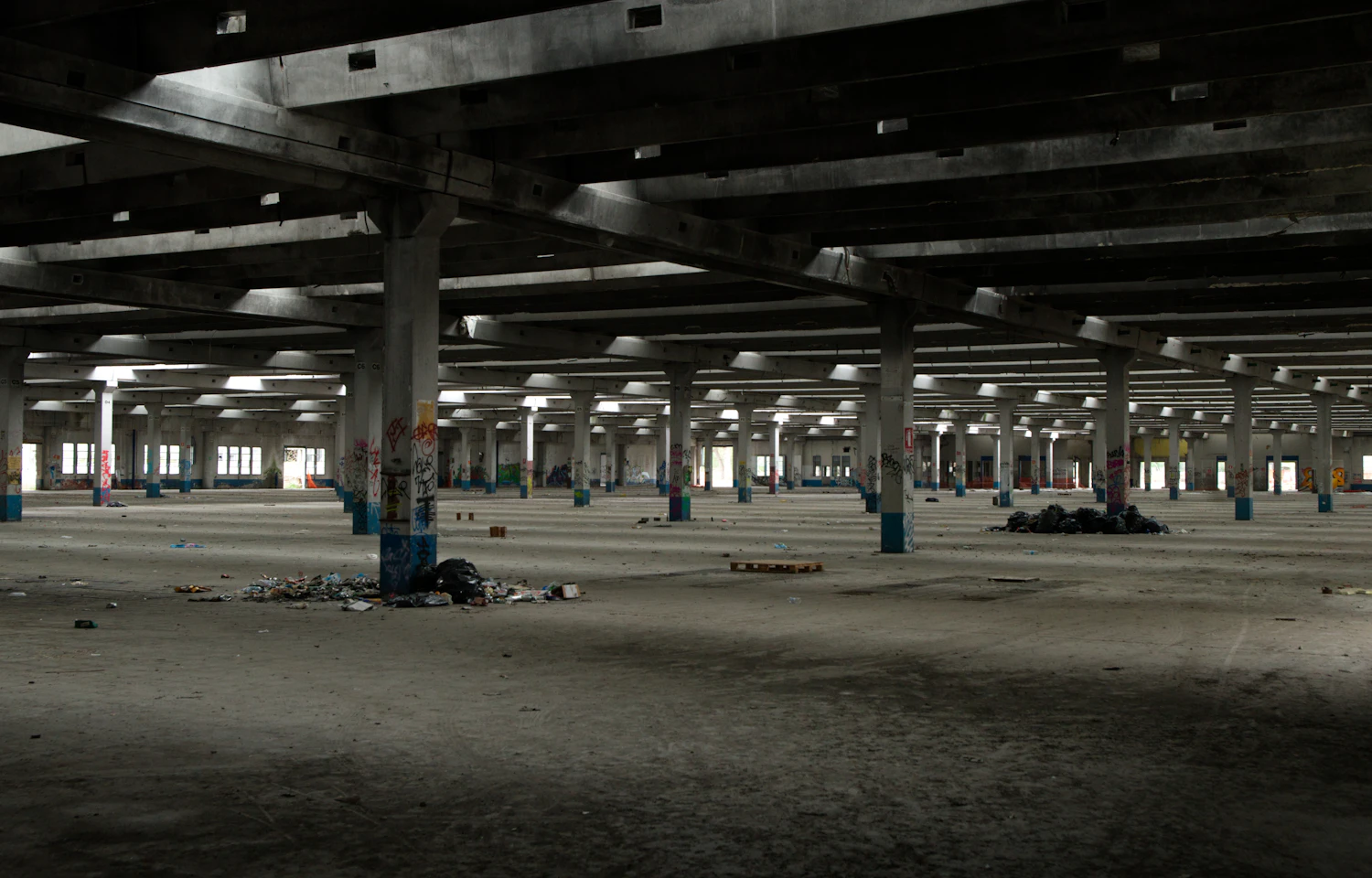 An empty concrete hall with square columns receding into shadow
