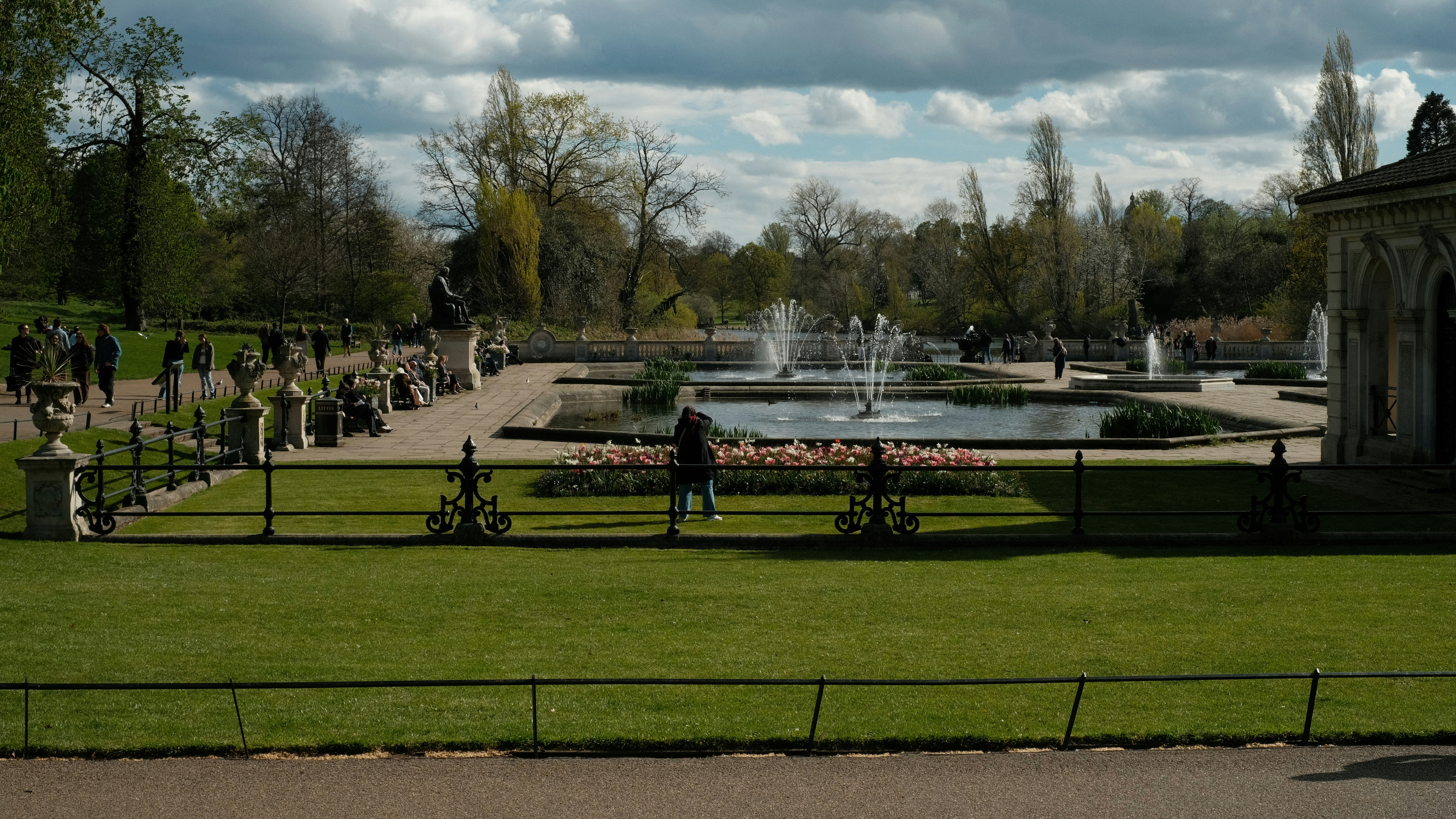 La gente pasea por un parque con una fuente.