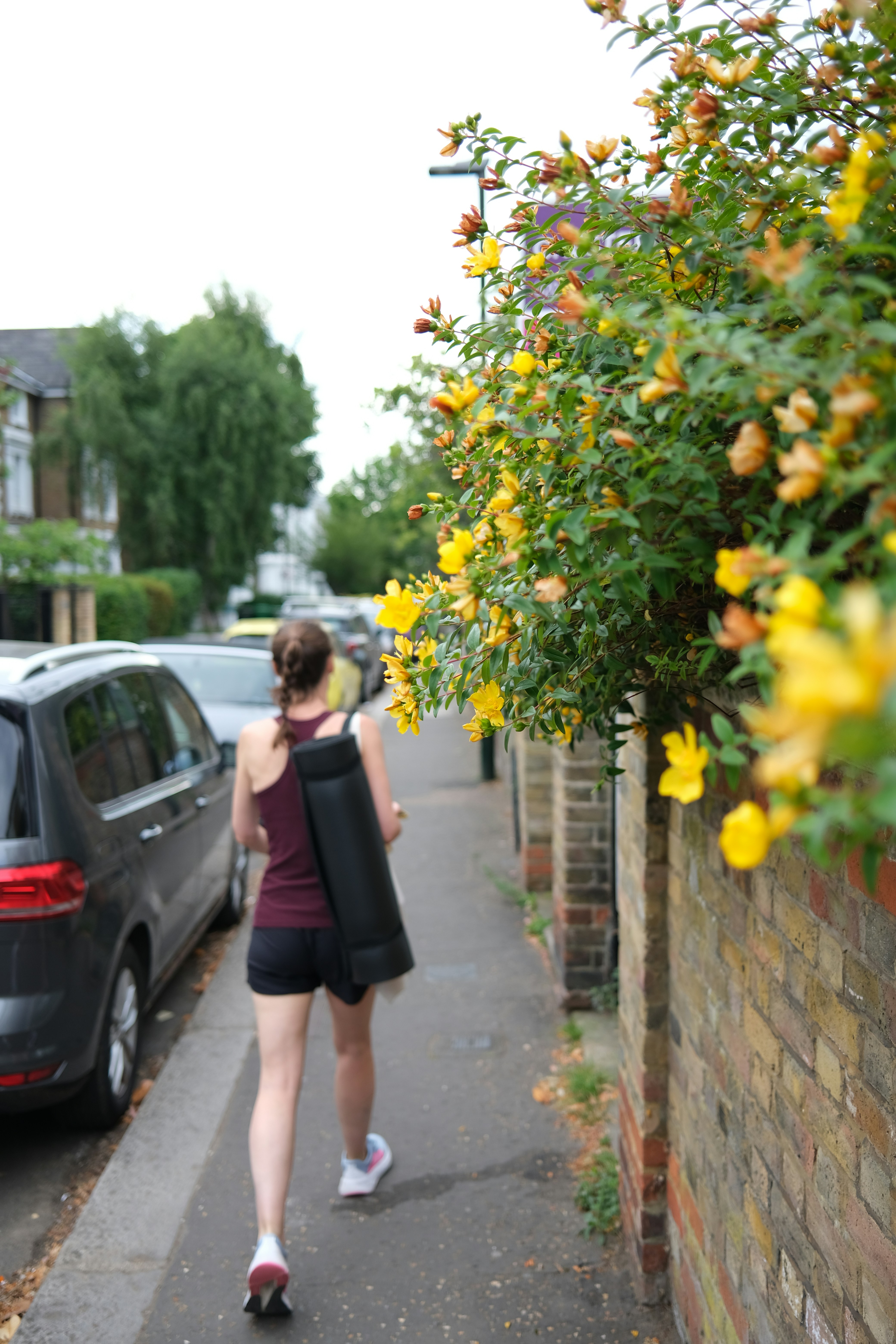 Woman walks down sidewalk carrying yoga mat