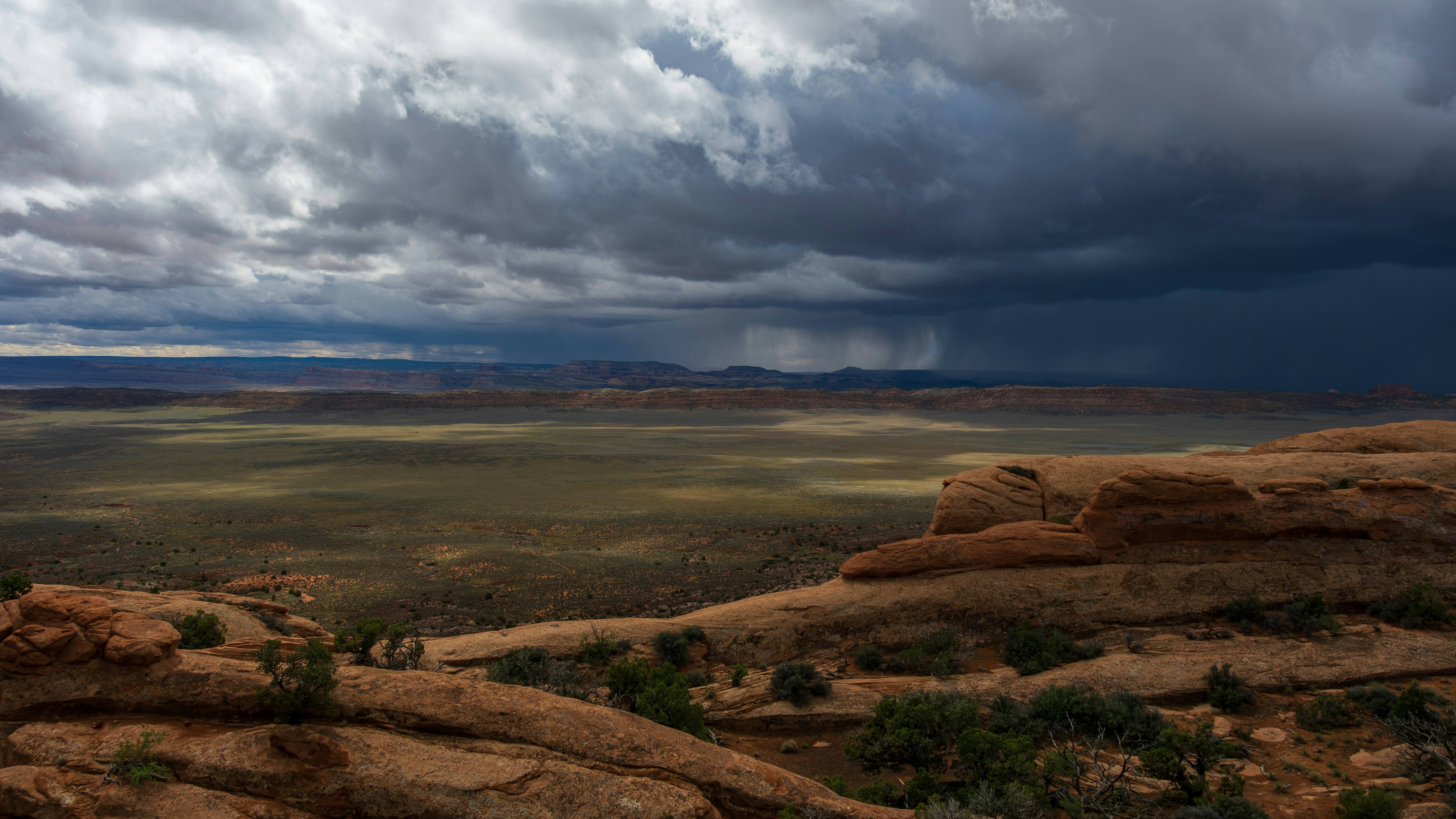 Storm clouds gather over a vast desert landscape.