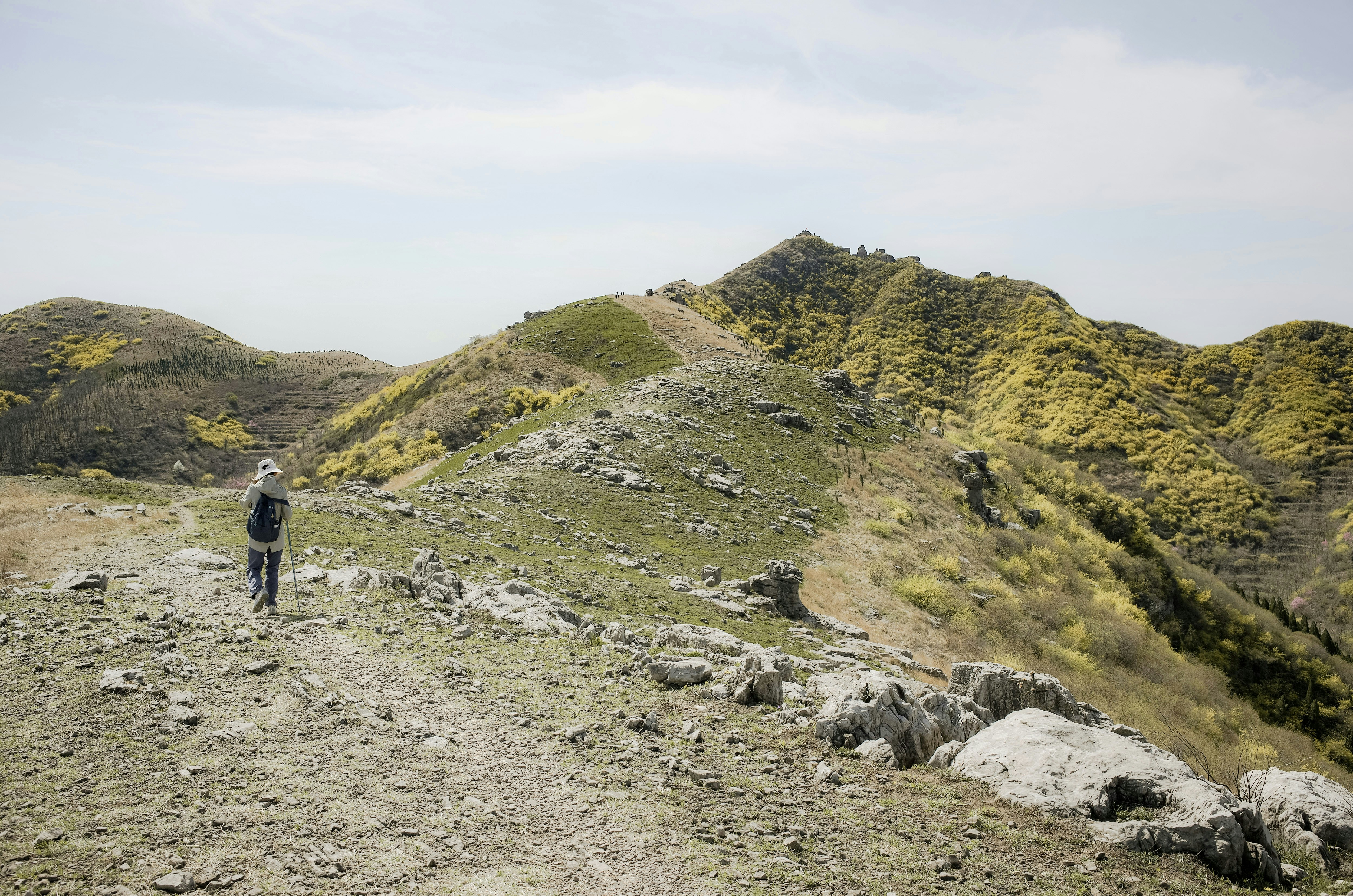 A person walks on a mountain path with green hills.