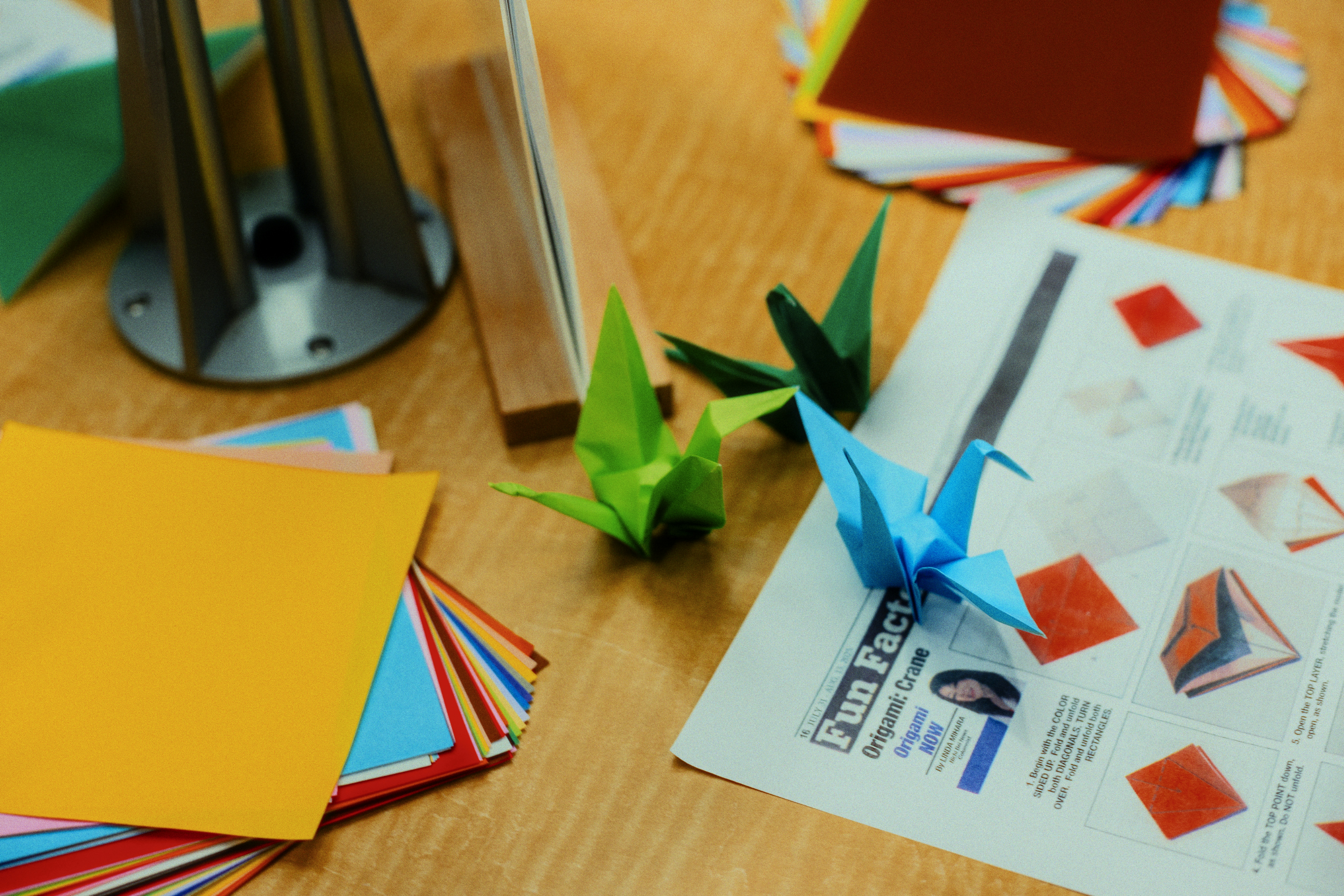 Bangau origami dan kertas warna-warni di atas meja.