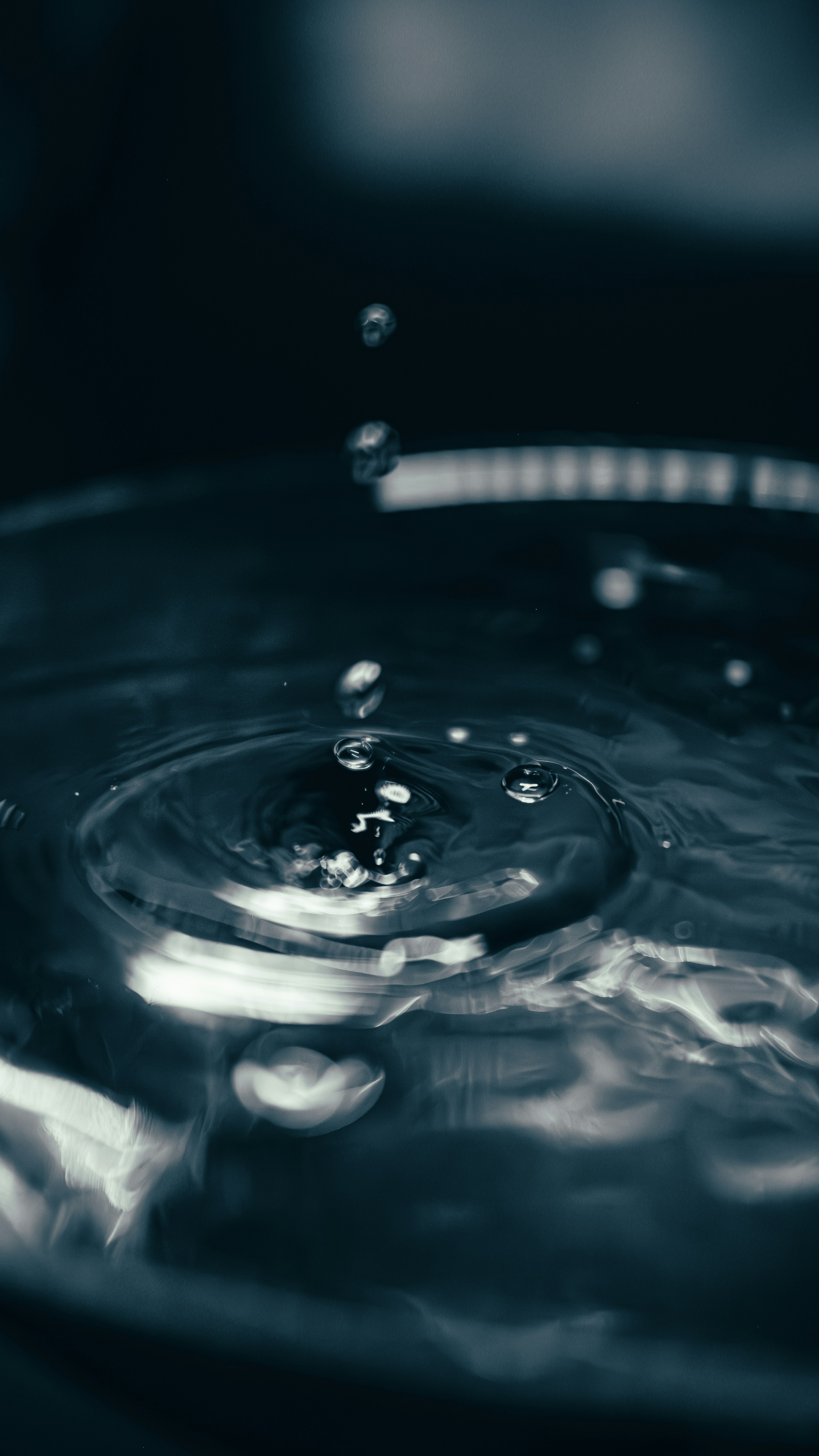 Wassertropfen, die in dunkles, welliges Wasser fallen.