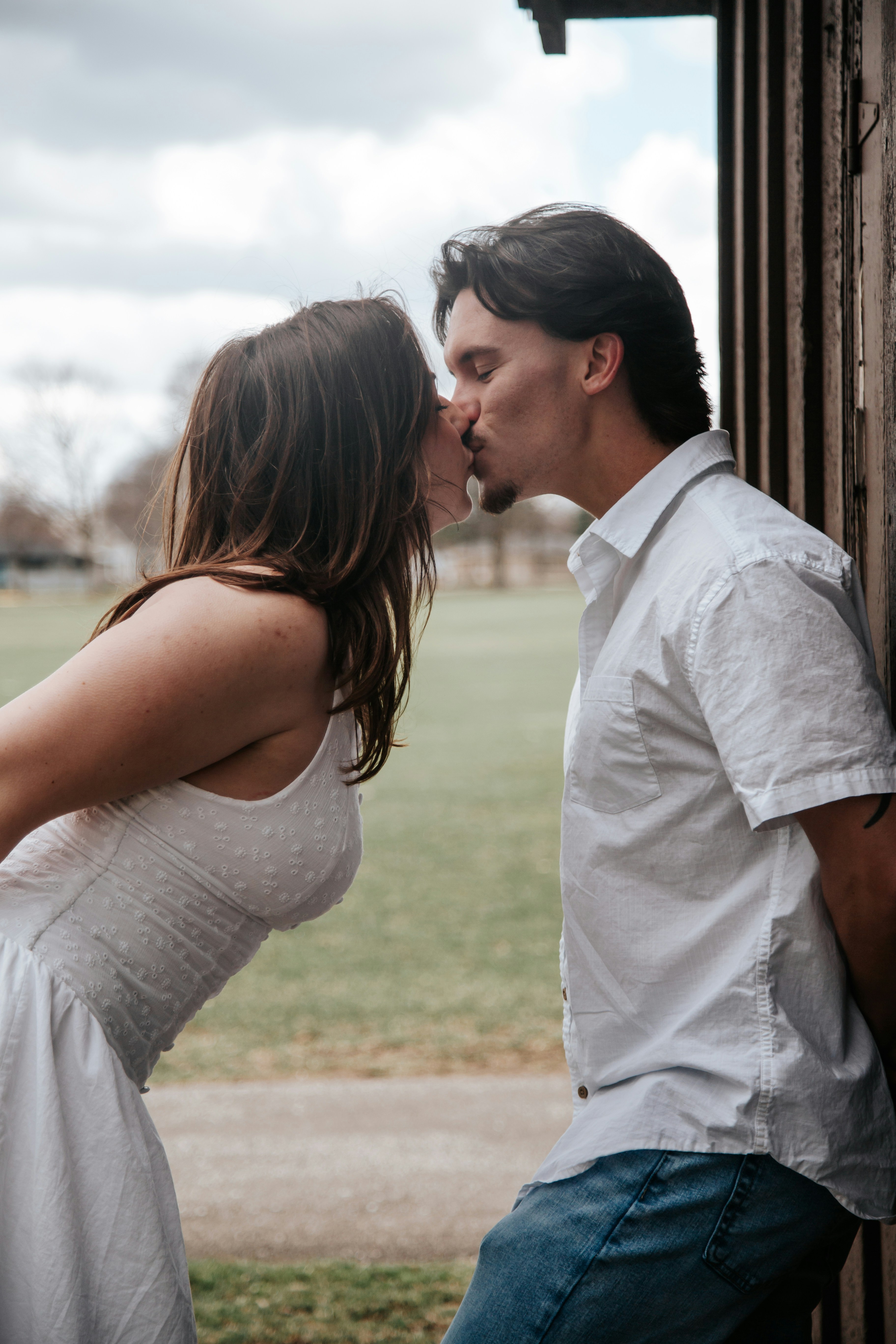 Casal se beijando ao ar livre perto de uma parede de madeira