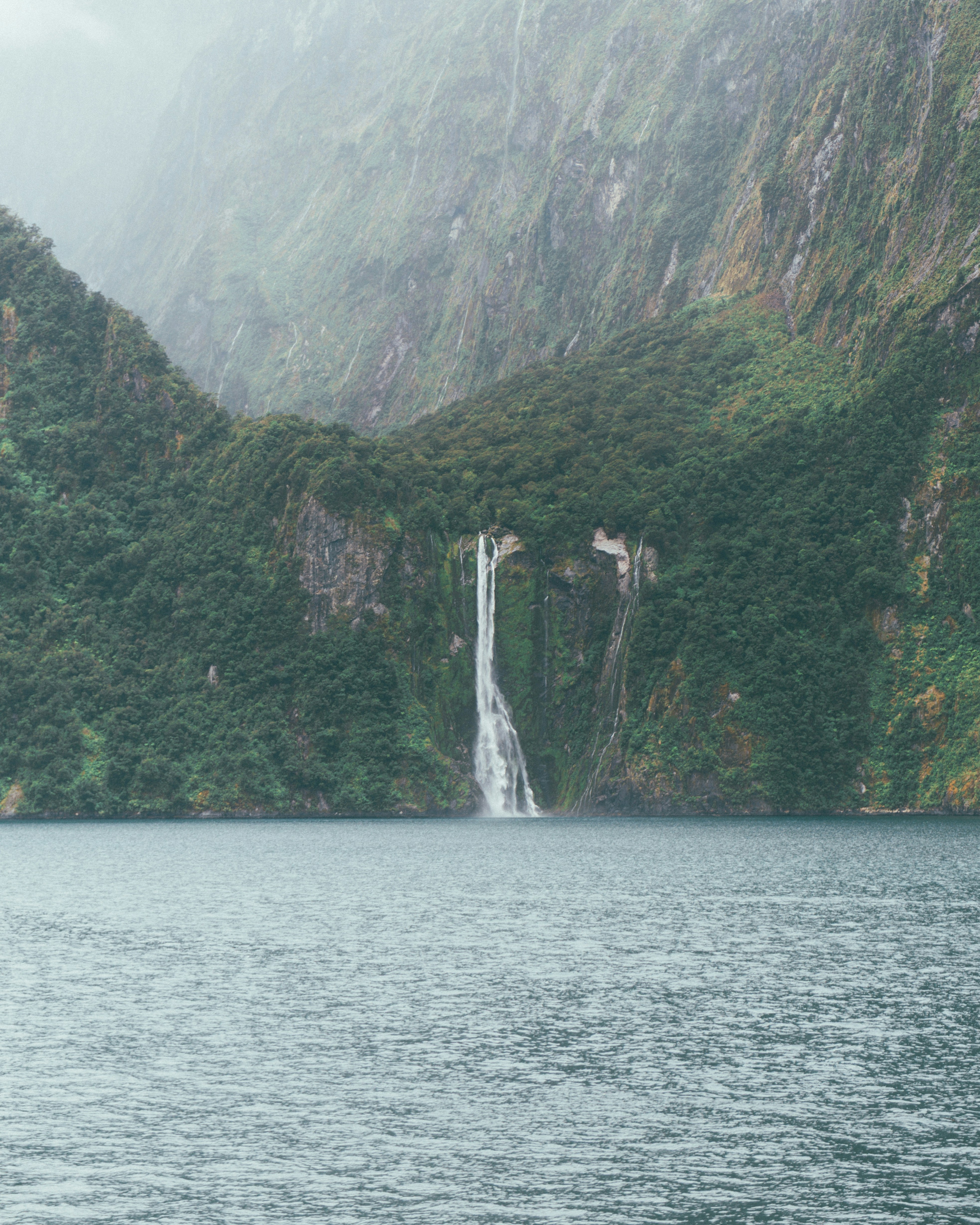 Waterfall cascading down a lush green mountainside into the ocean.