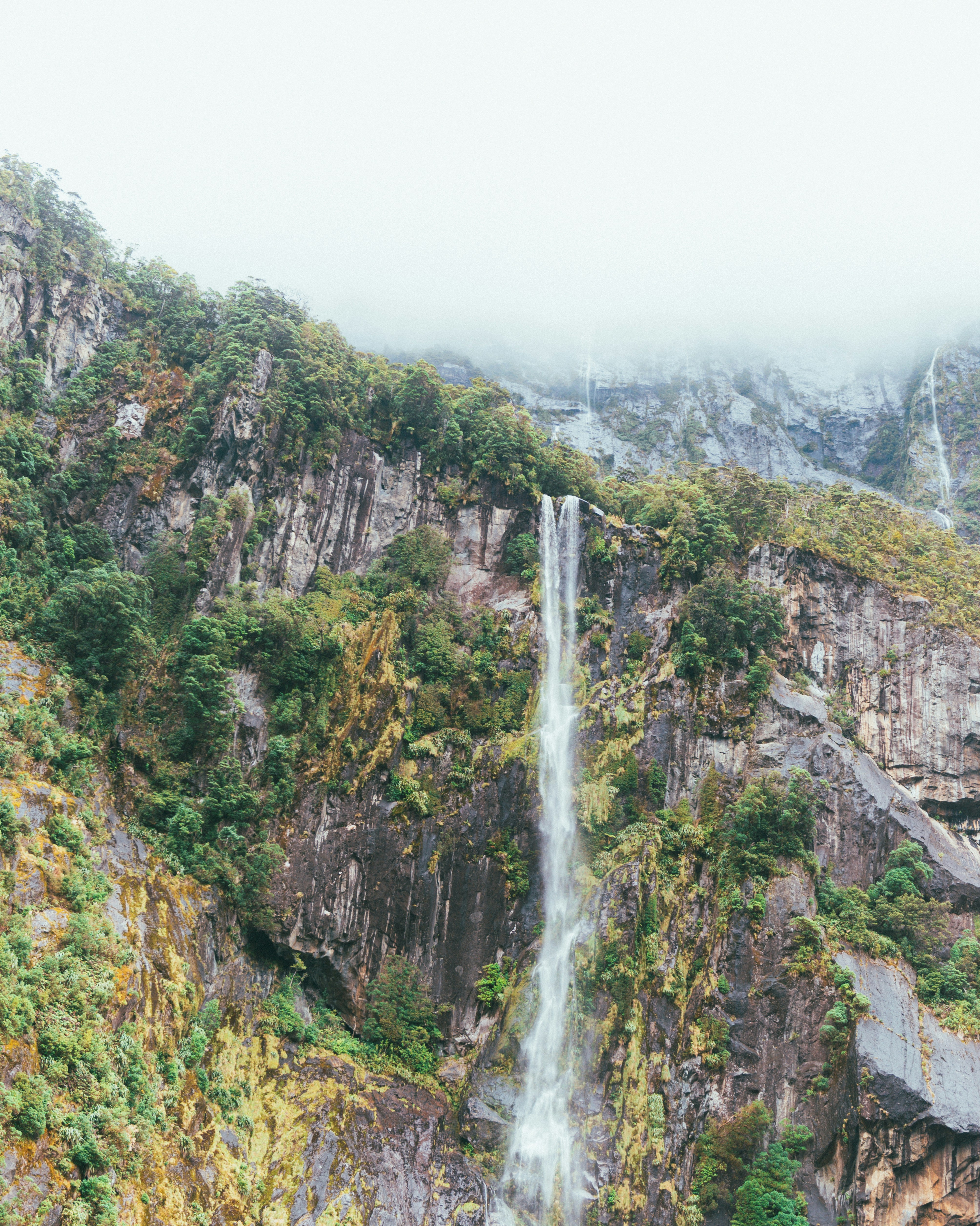 A tall waterfall cascades down a lush, rocky mountainside.