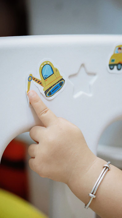 A child's hand touches a sticker of a yellow excavator.