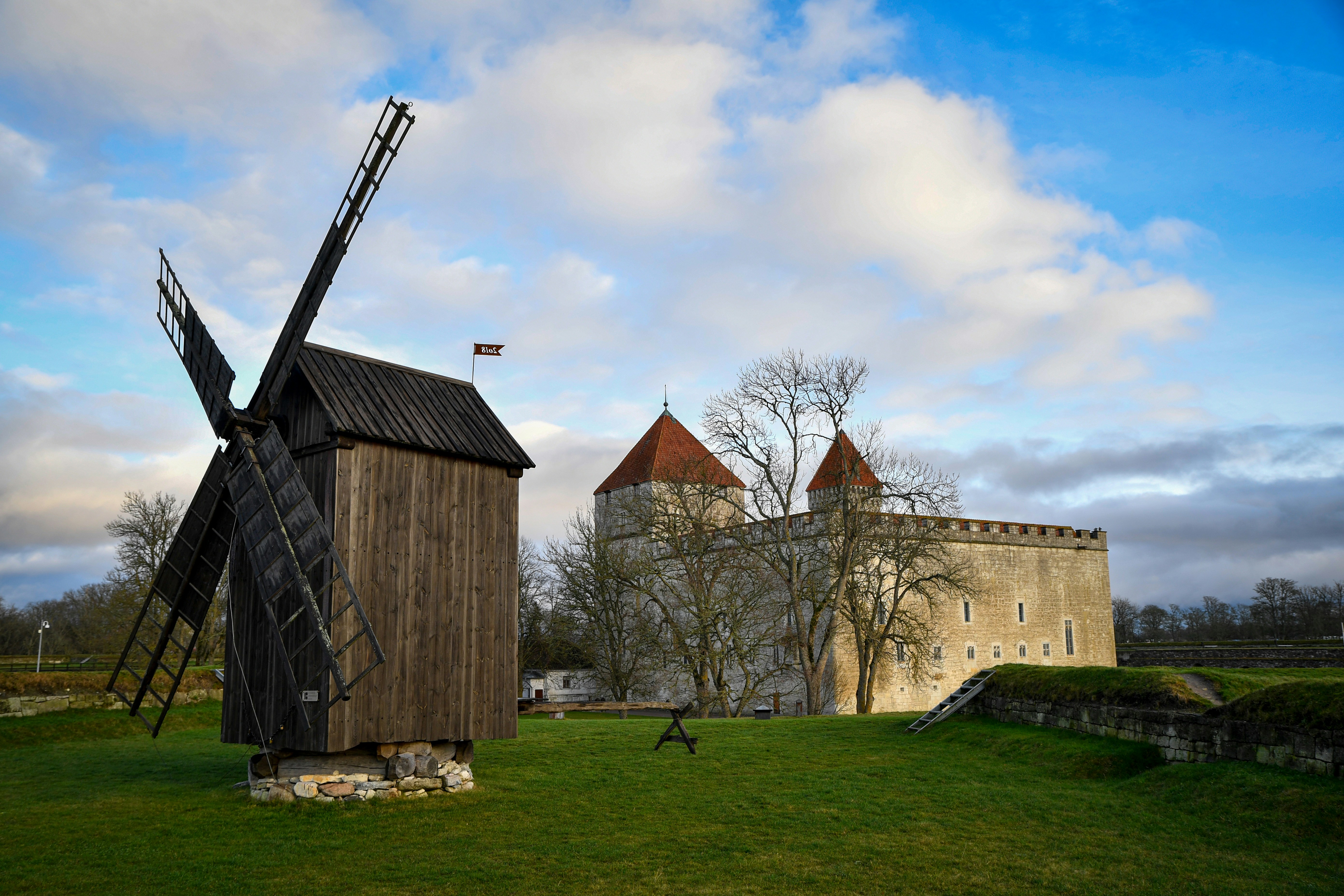 Old wooden windmill in front of a stone castle