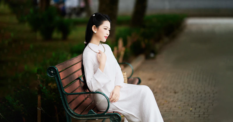 young woman in a white dress sitting on a park bench