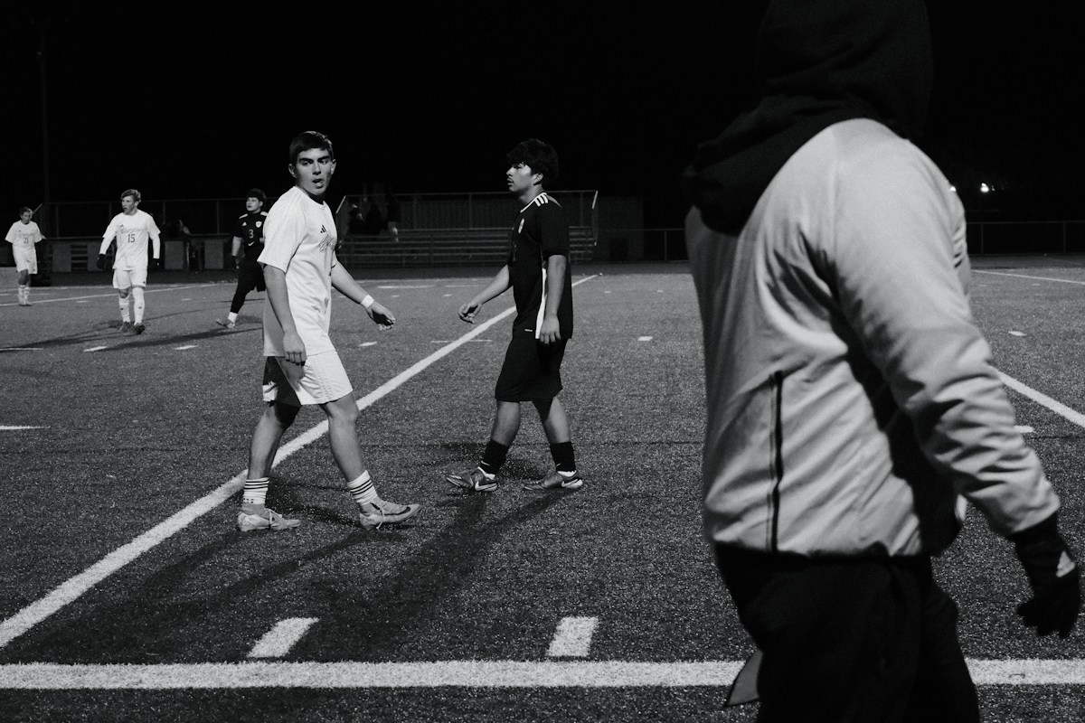 Young men playing soccer on a lit field at night, illustrating youth sports activities.