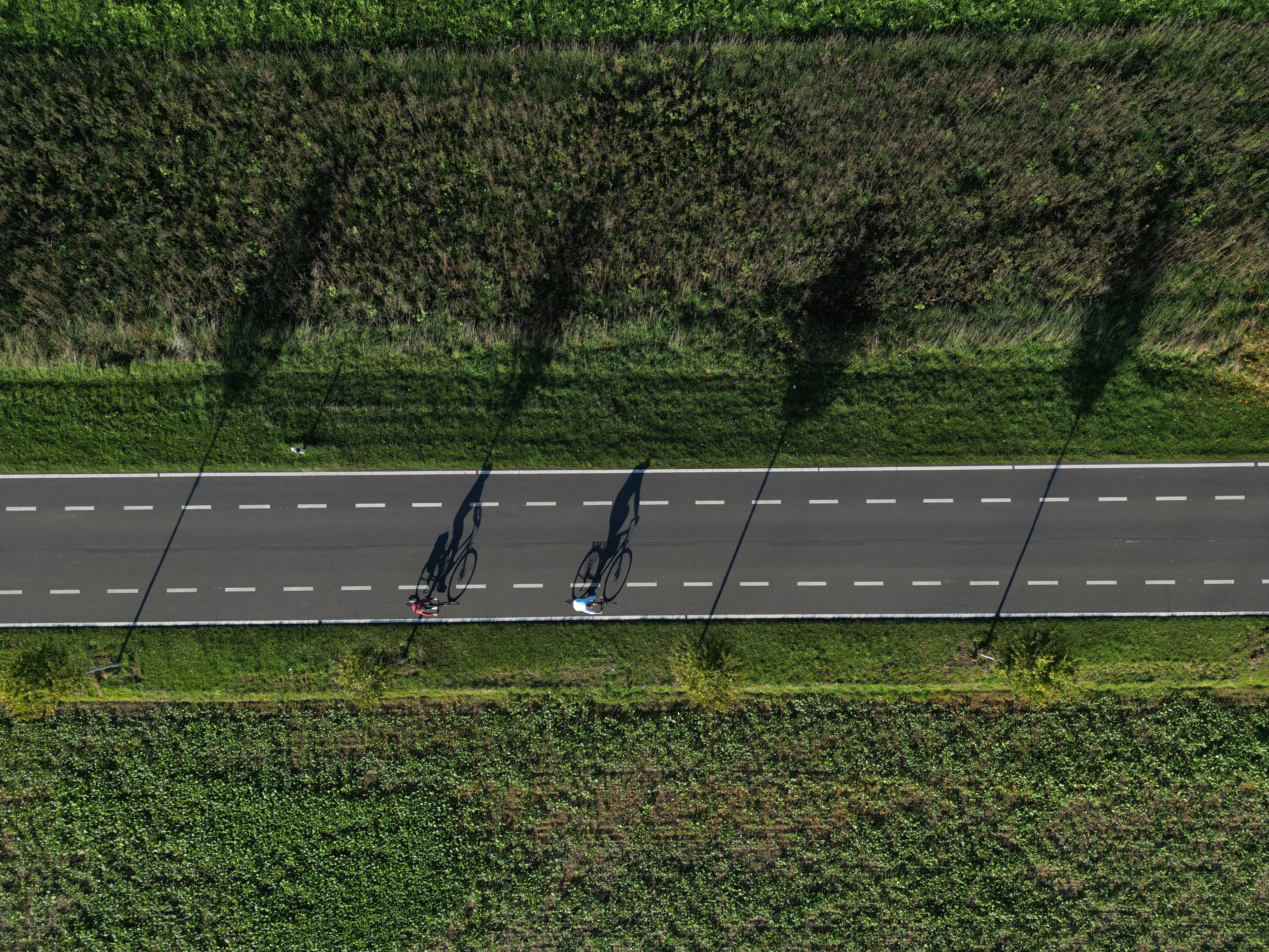 Two cyclists ride on a country road during daytime.