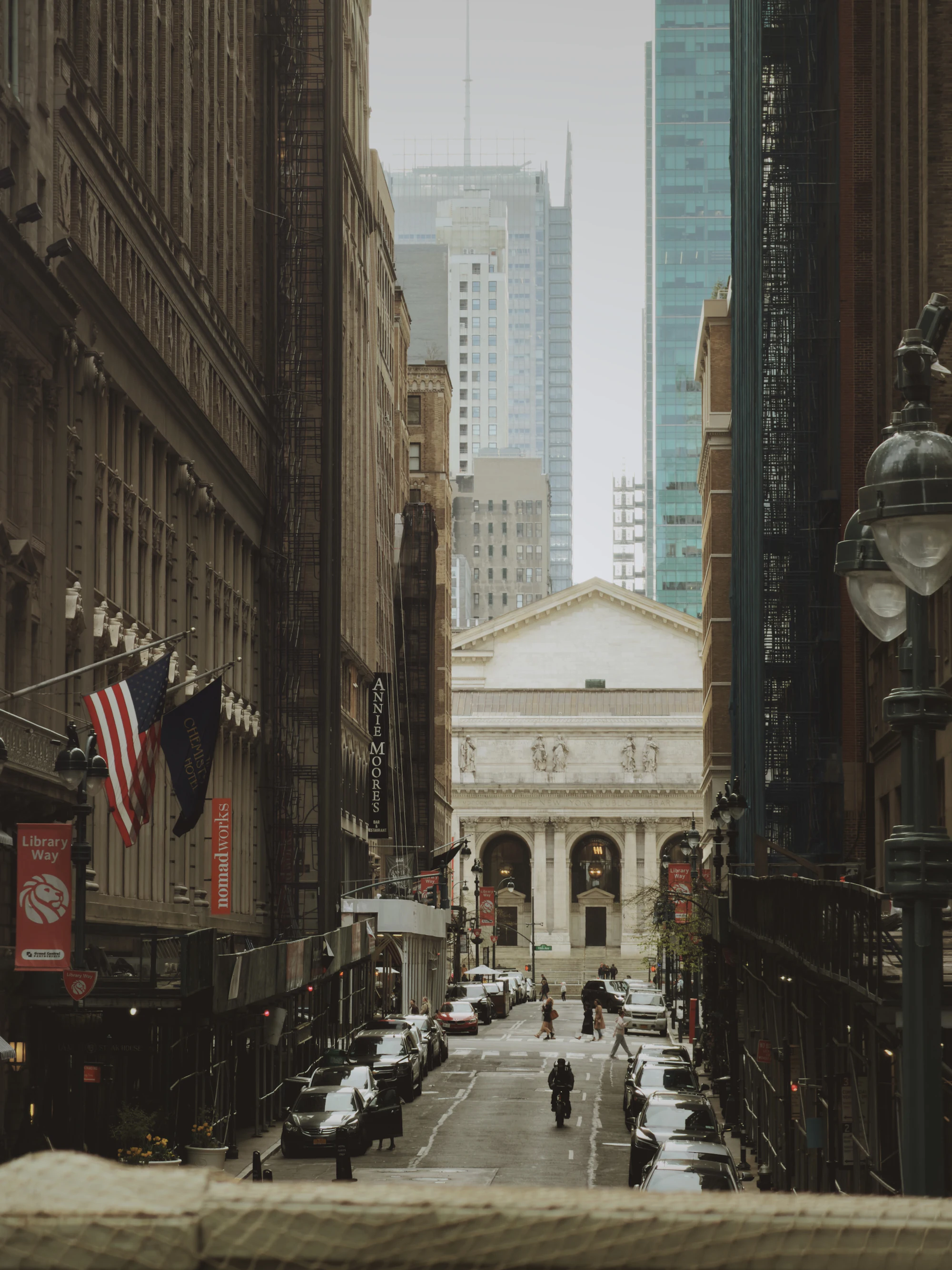 A New York City street where classical architecture meets modern buildings, an American flag in view.