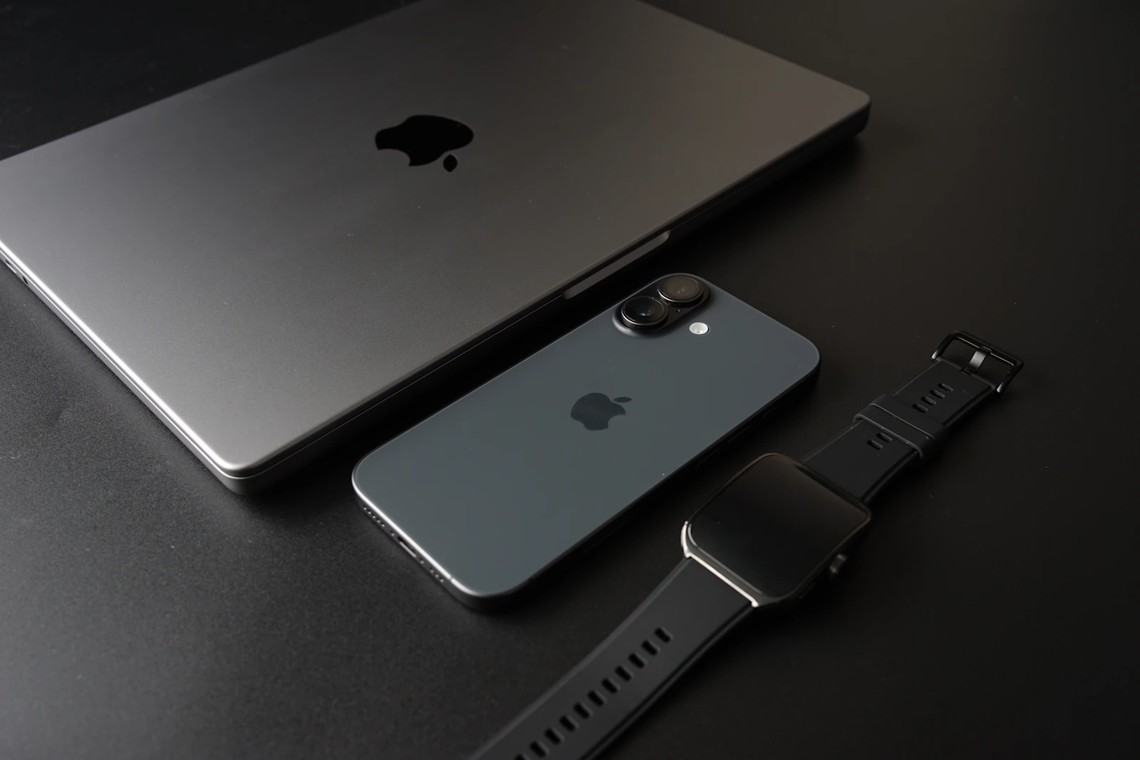 Laptop, smartphone and smartwatch arranged together on a dark surface