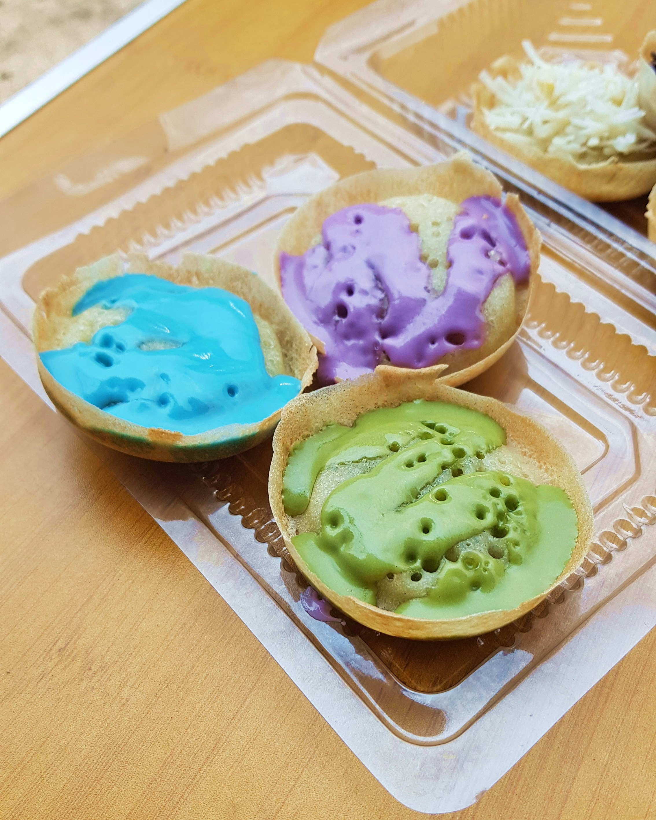 Tiga panekuk warna-warni dengan topping dalam wadah.