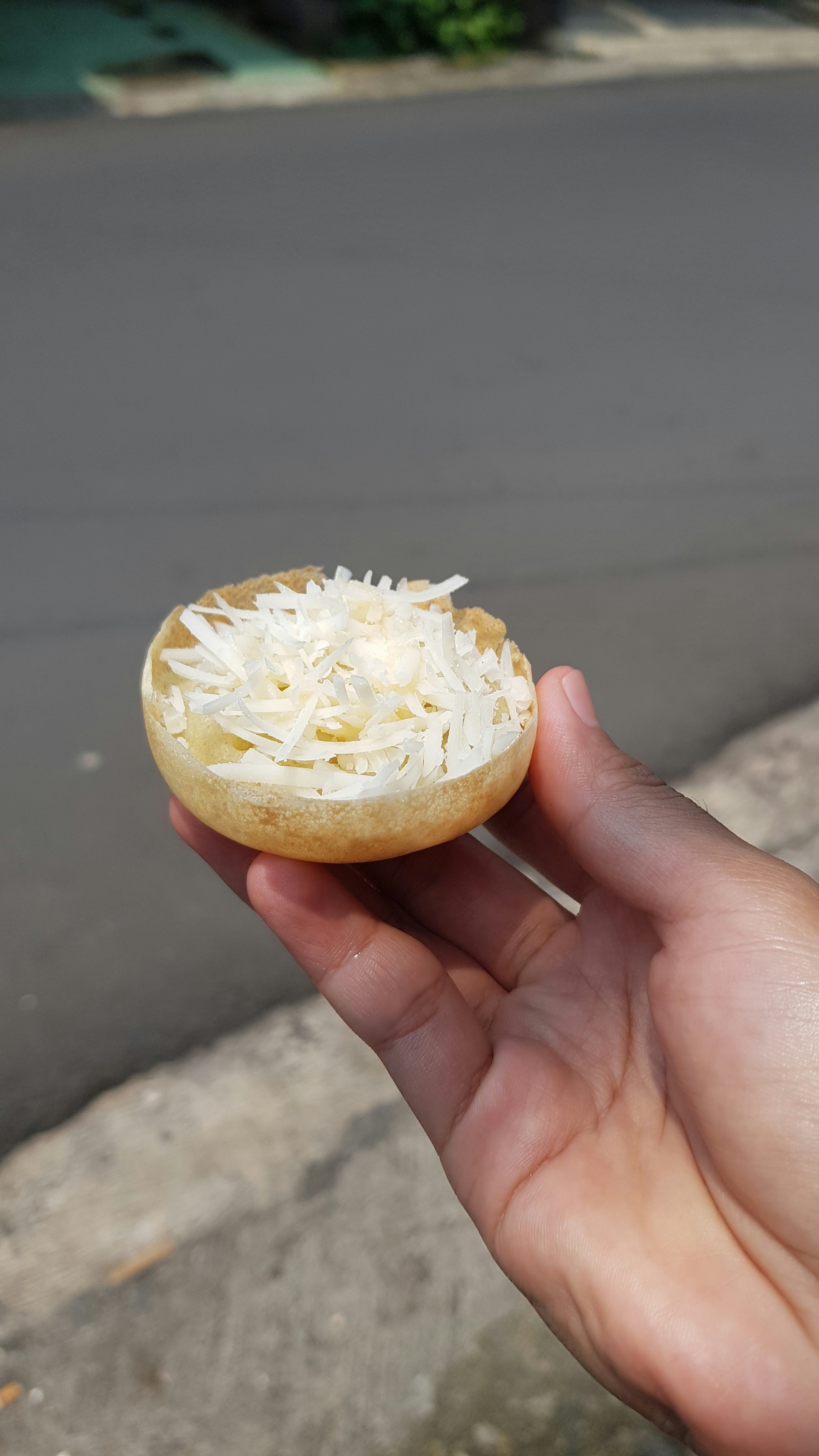Tangan memegang buah berlubang yang diisi dengan keju parut.
