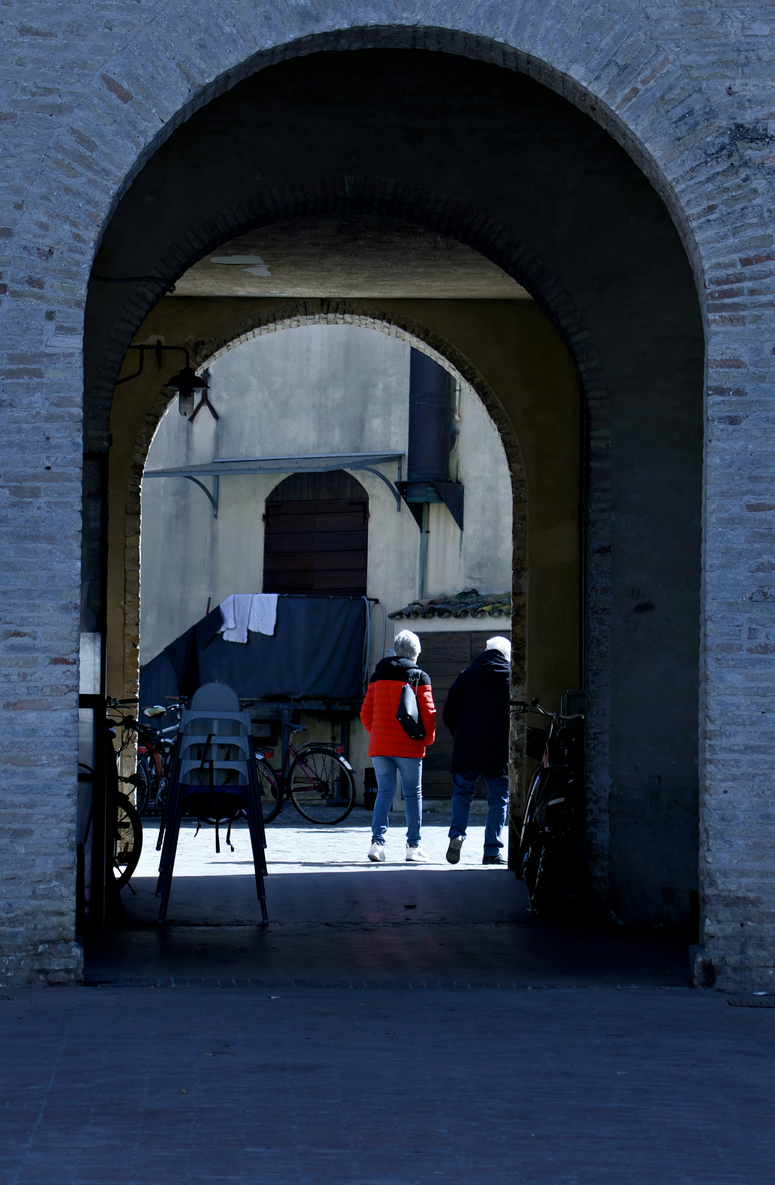 Two people walk through an arched passageway.
