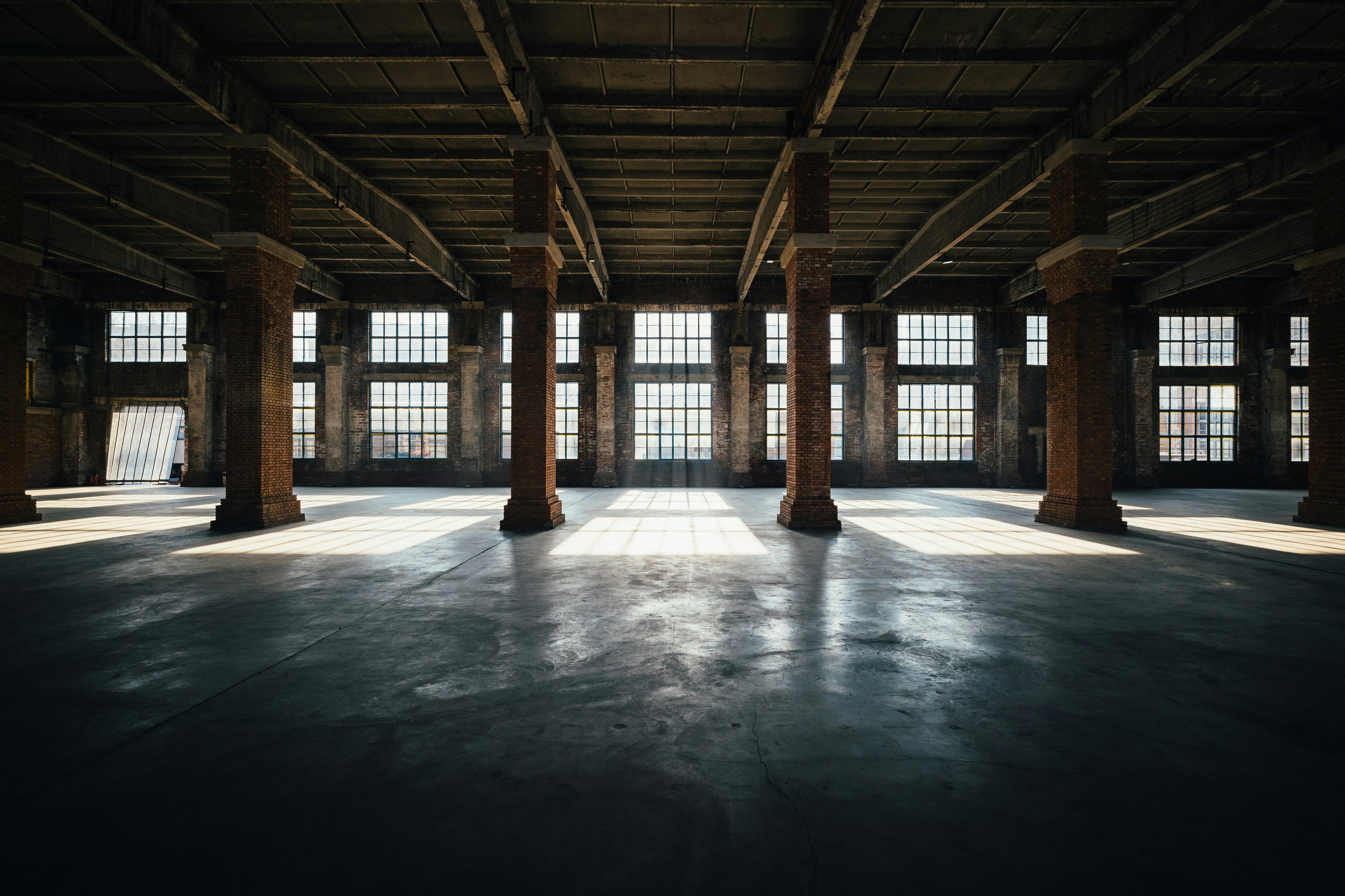 Sunlight streams into an empty industrial warehouse interior.