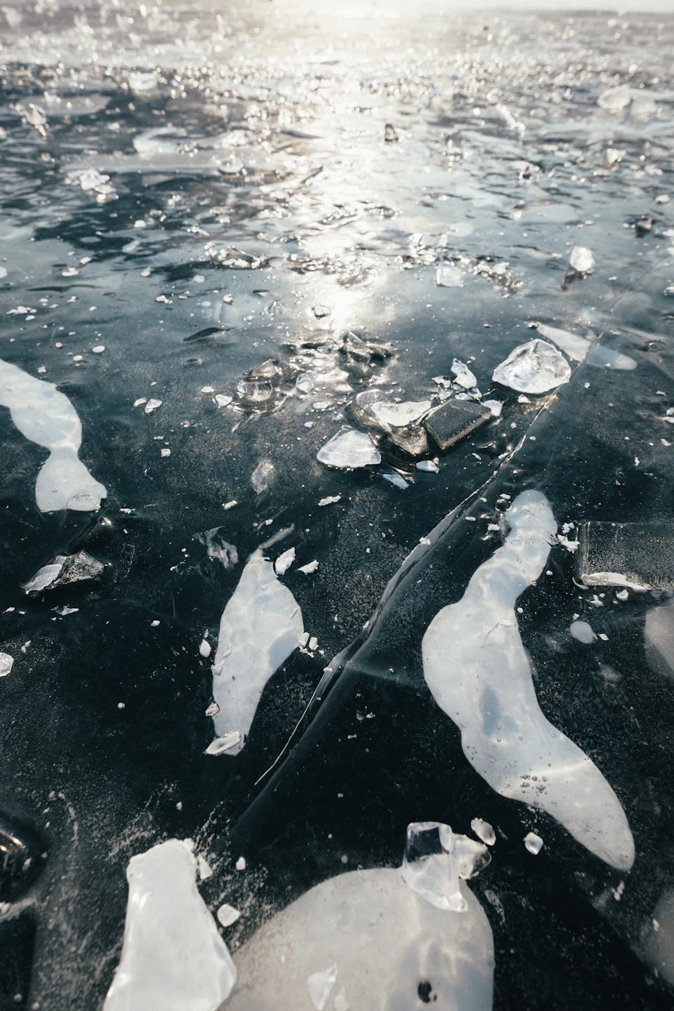 Frozen lake with intricate pattern of ice crystals reflecting surrounding environment under sunlight