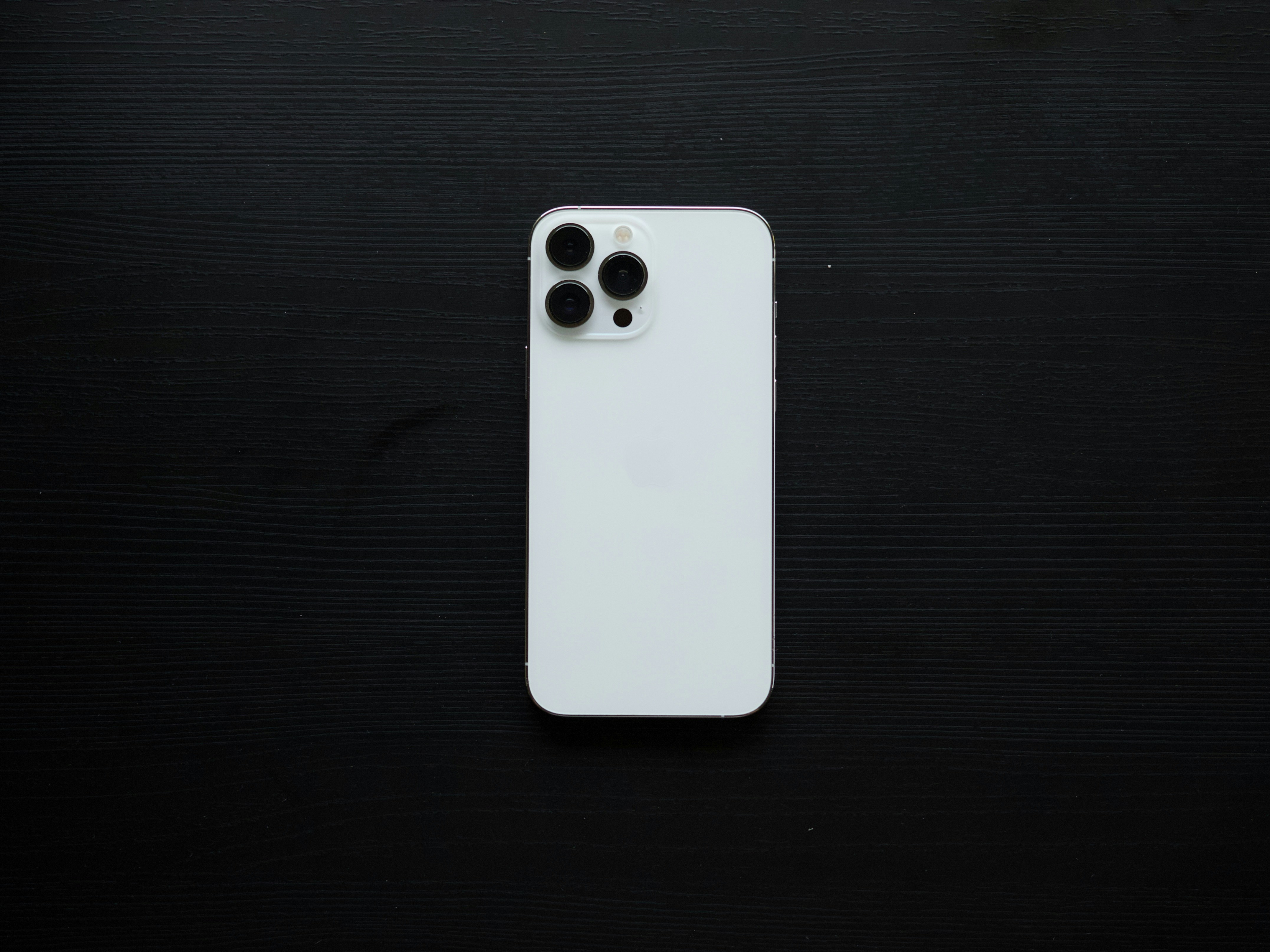 Un smartphone blanco descansa sobre una superficie de madera negra.