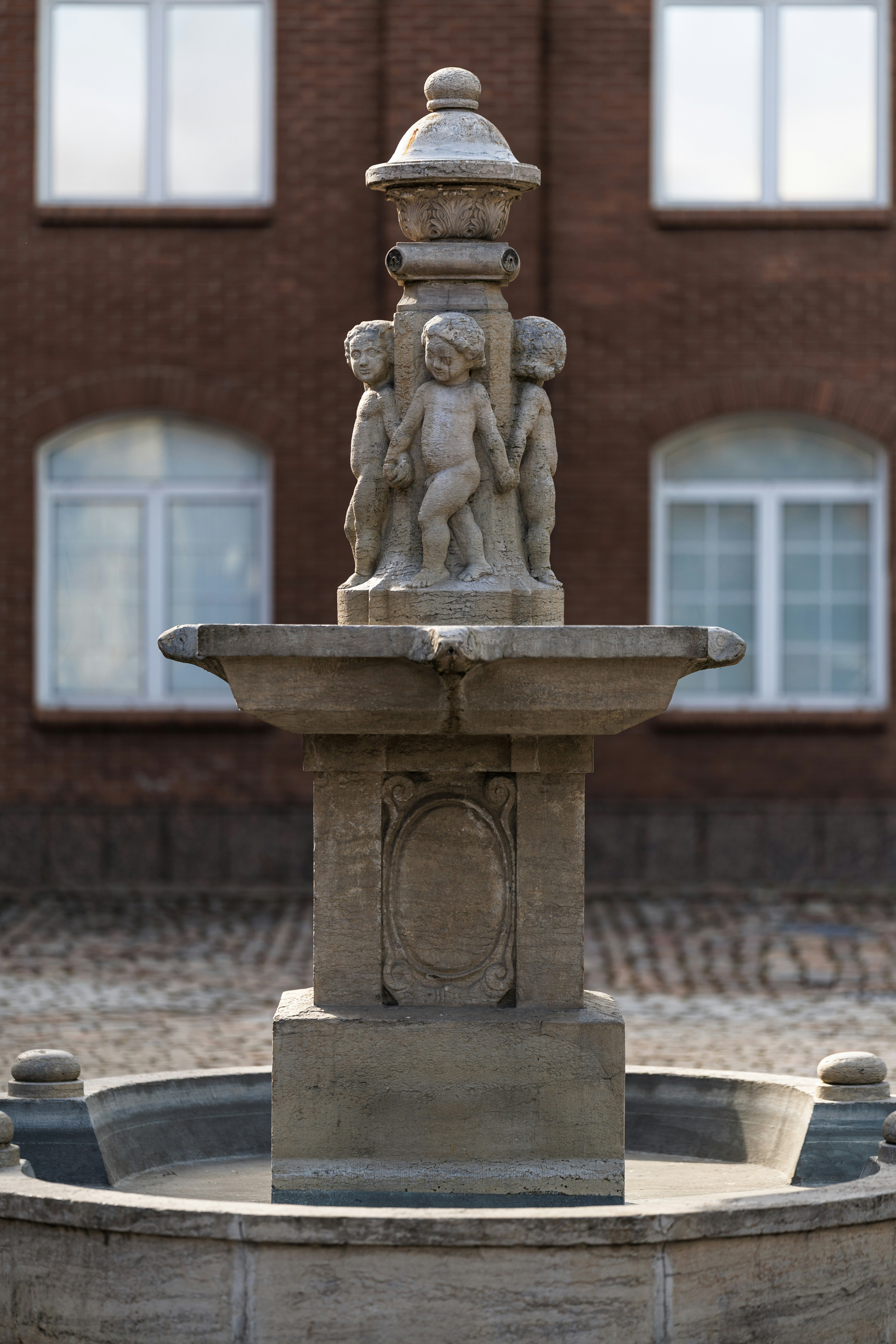 Stone fountain with cherubs in front of brick building