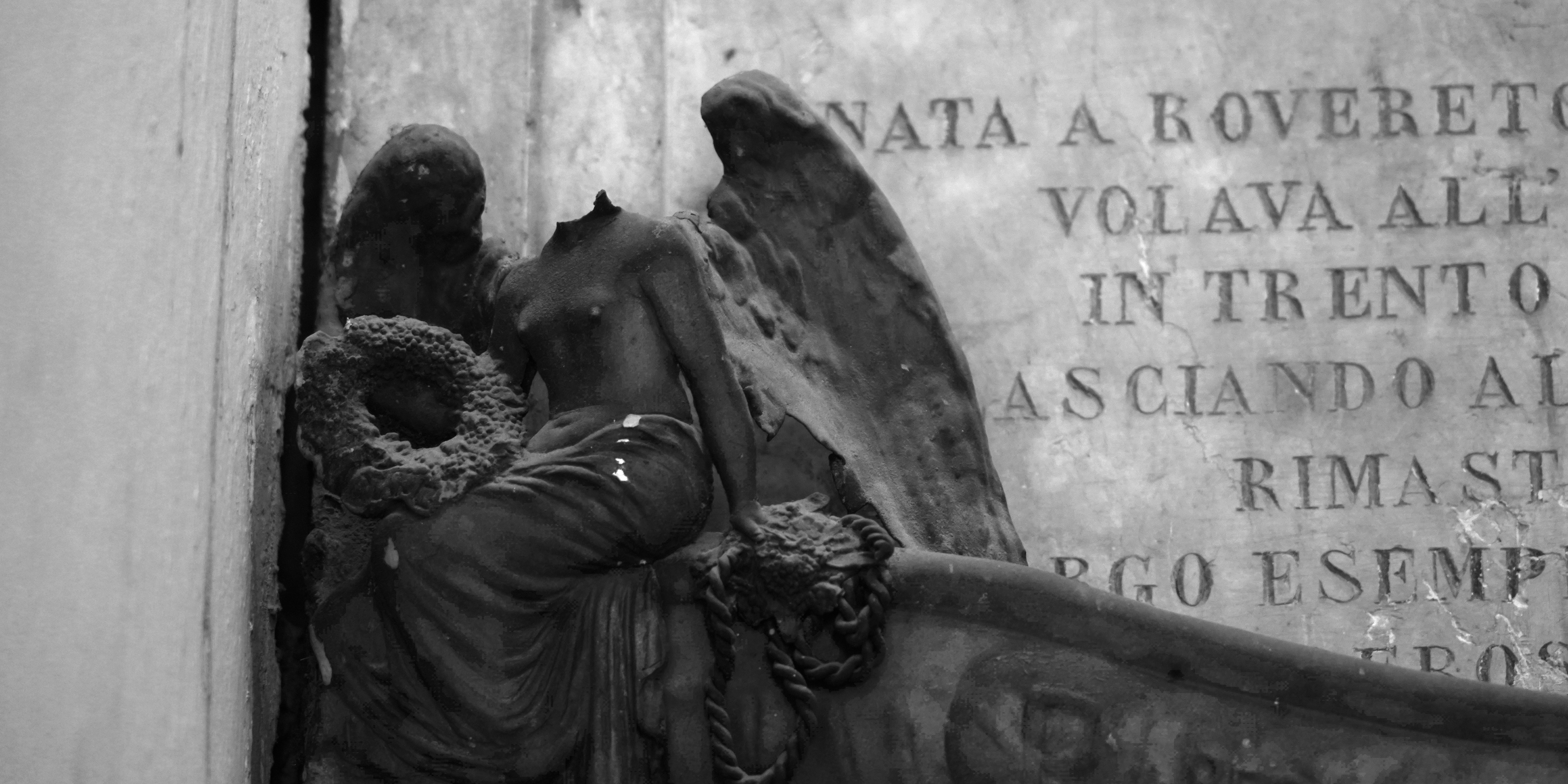 Headless angel sculpture with wreath and inscription.