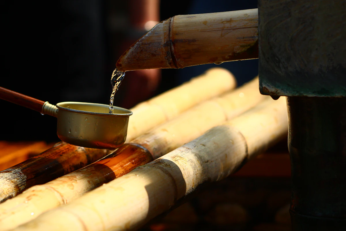 Water flowing from bamboo spout into a metal ladle at a Japanese Shinto shrine purification fountain