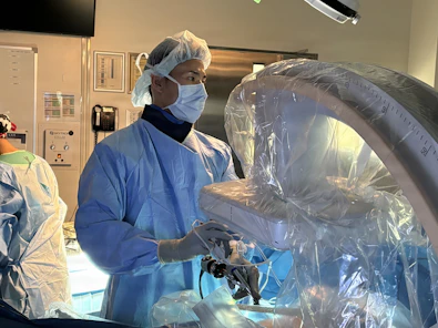 Surgeon in mask operating robotic surgical equipment in operating room