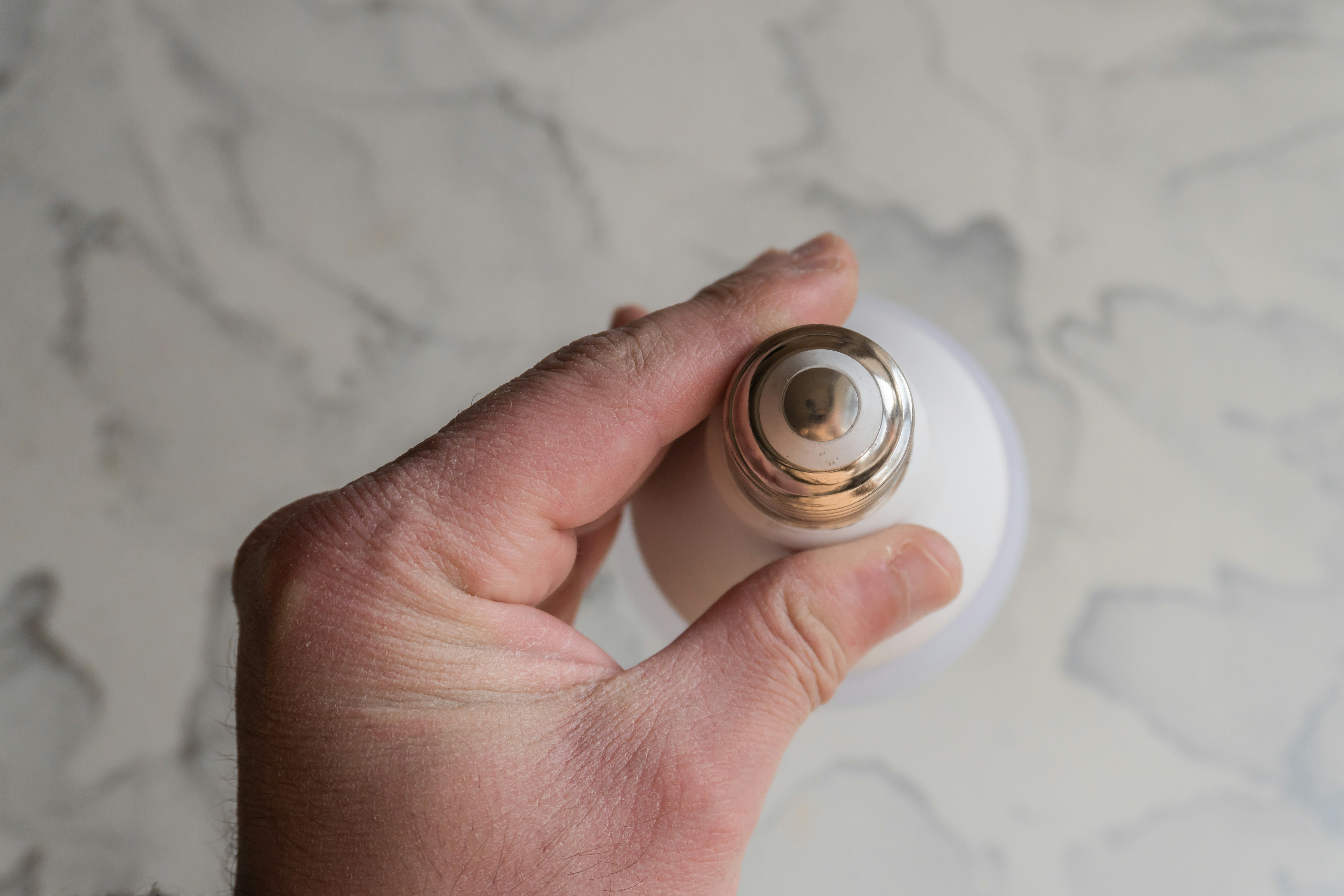 Hand holding a white bottle with a gold cap.