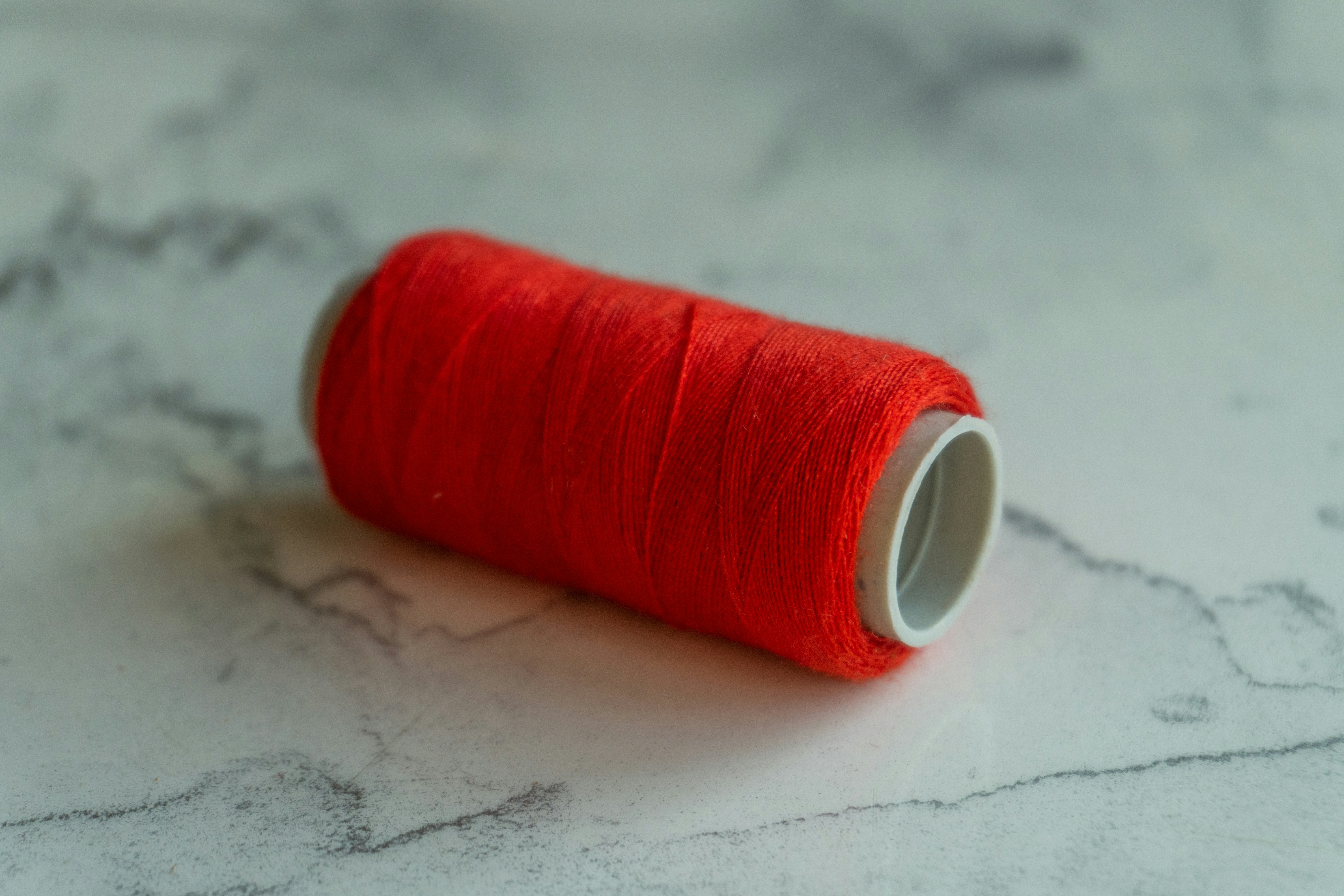 A spool of bright red thread on a marbled surface.
