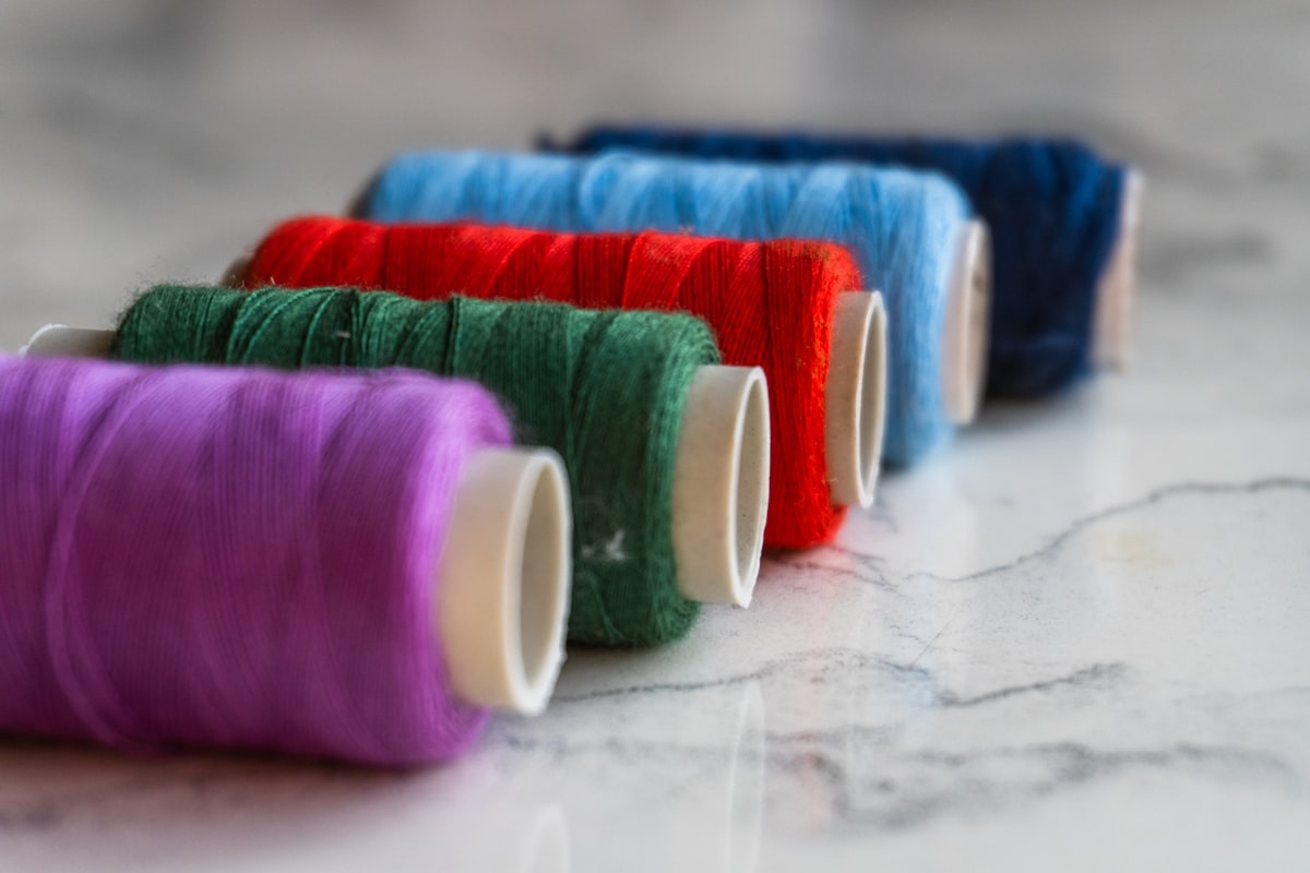 ring-spun vs combed cotton t-shirts — colorful thread spools on a wooden surface showing different yarn types used in textile production