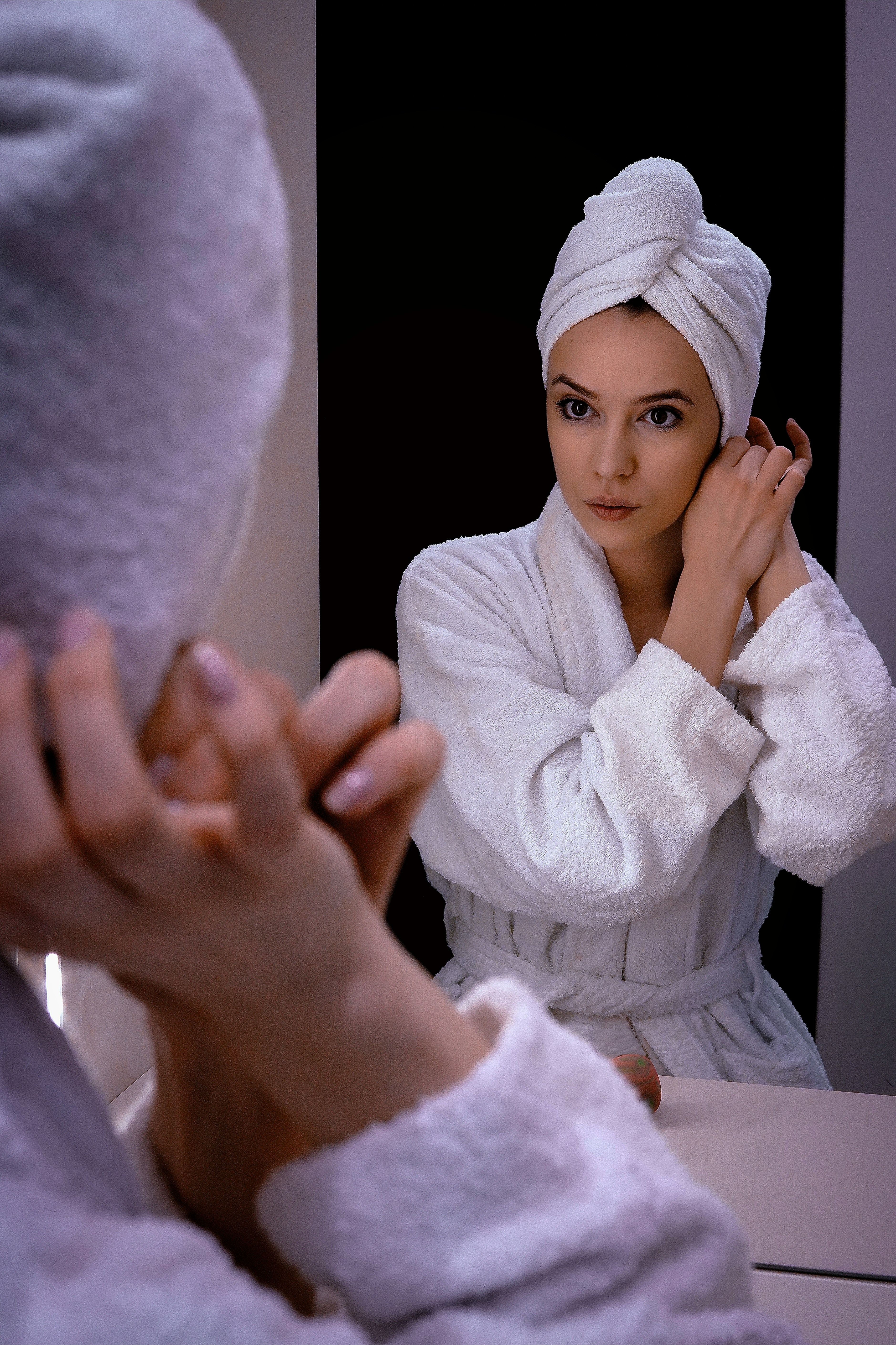 Wanita berjubah mandi dan handuk menyesuaikan anting-anting di cermin.