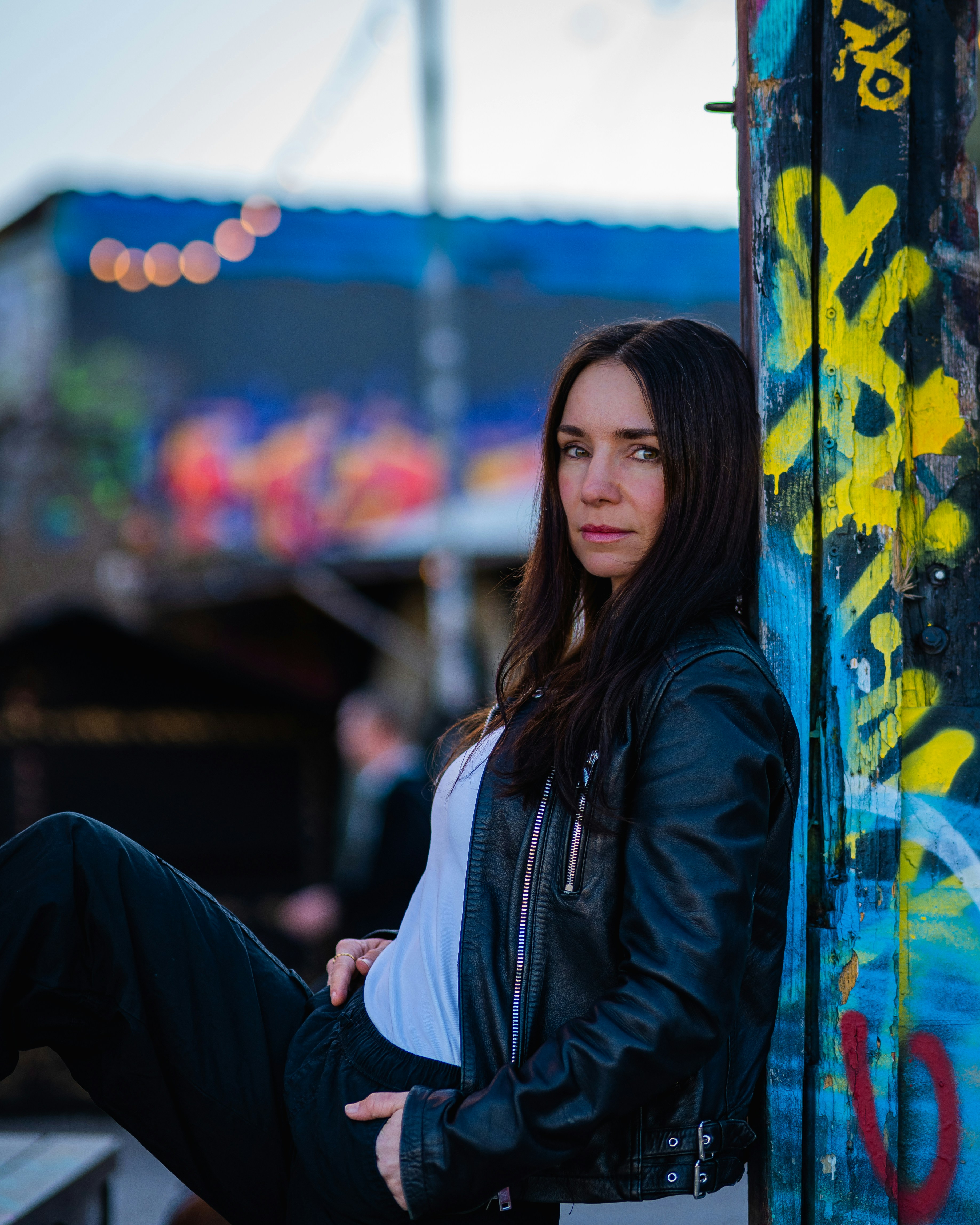 Woman in leather jacket leaning against graffiti wall