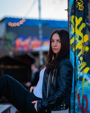 Woman in leather jacket leaning against graffiti wall