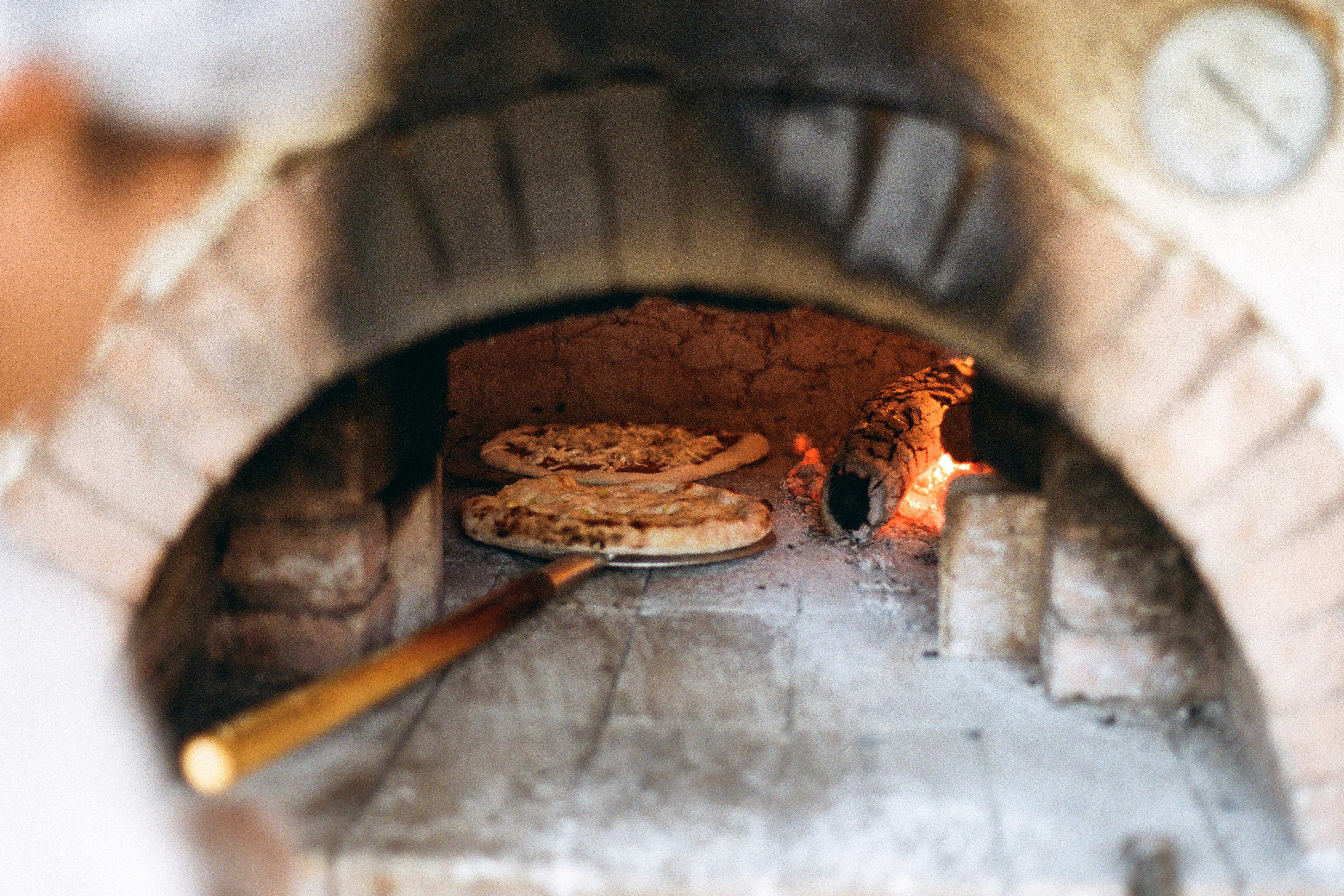 Pizza baking in a wood-fired oven with a peel