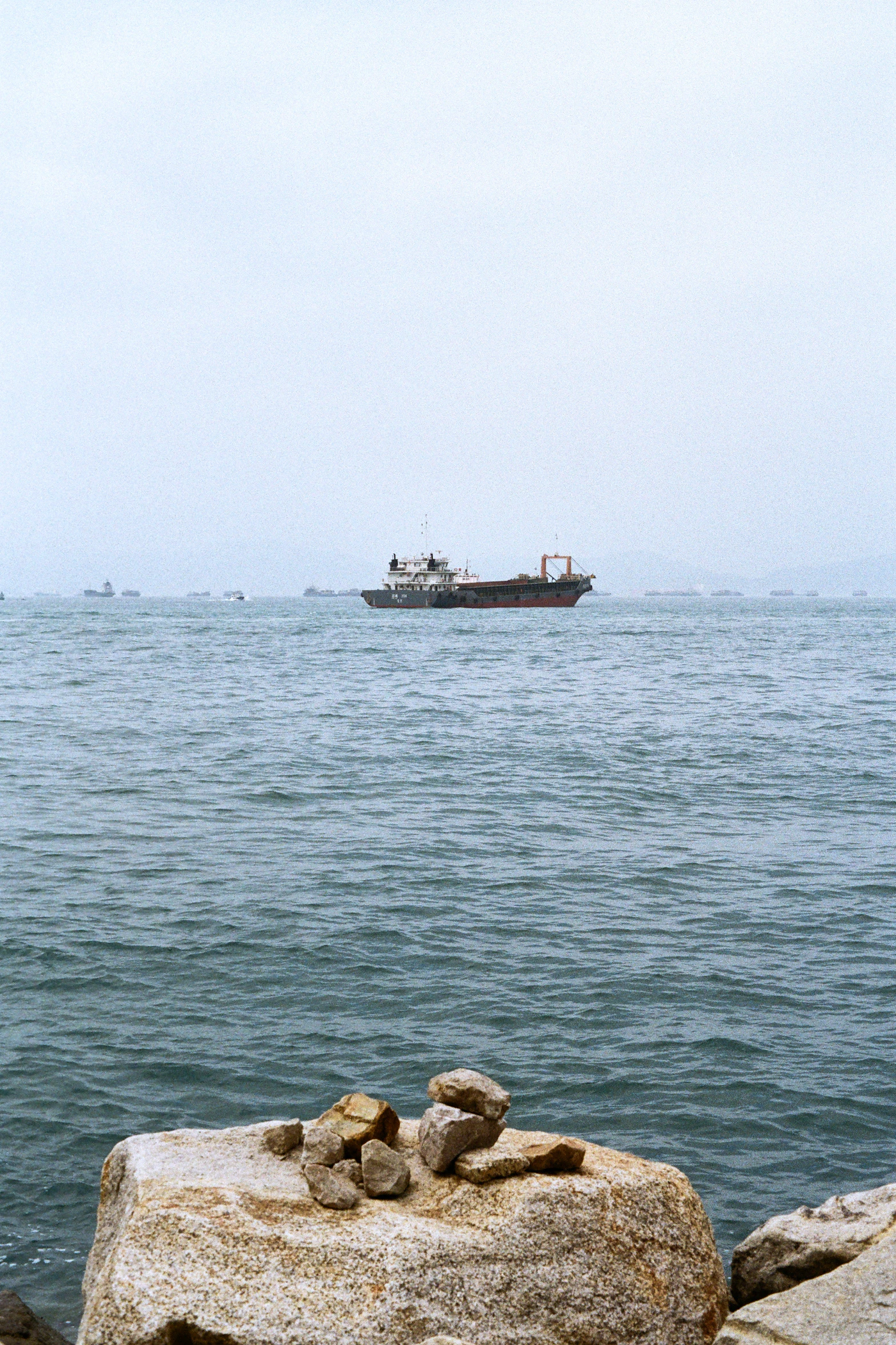 Cargo ship at sea with a rocky coast in the foreground on a bright day, representing the deadlines and evidence issues in a high seas death claim