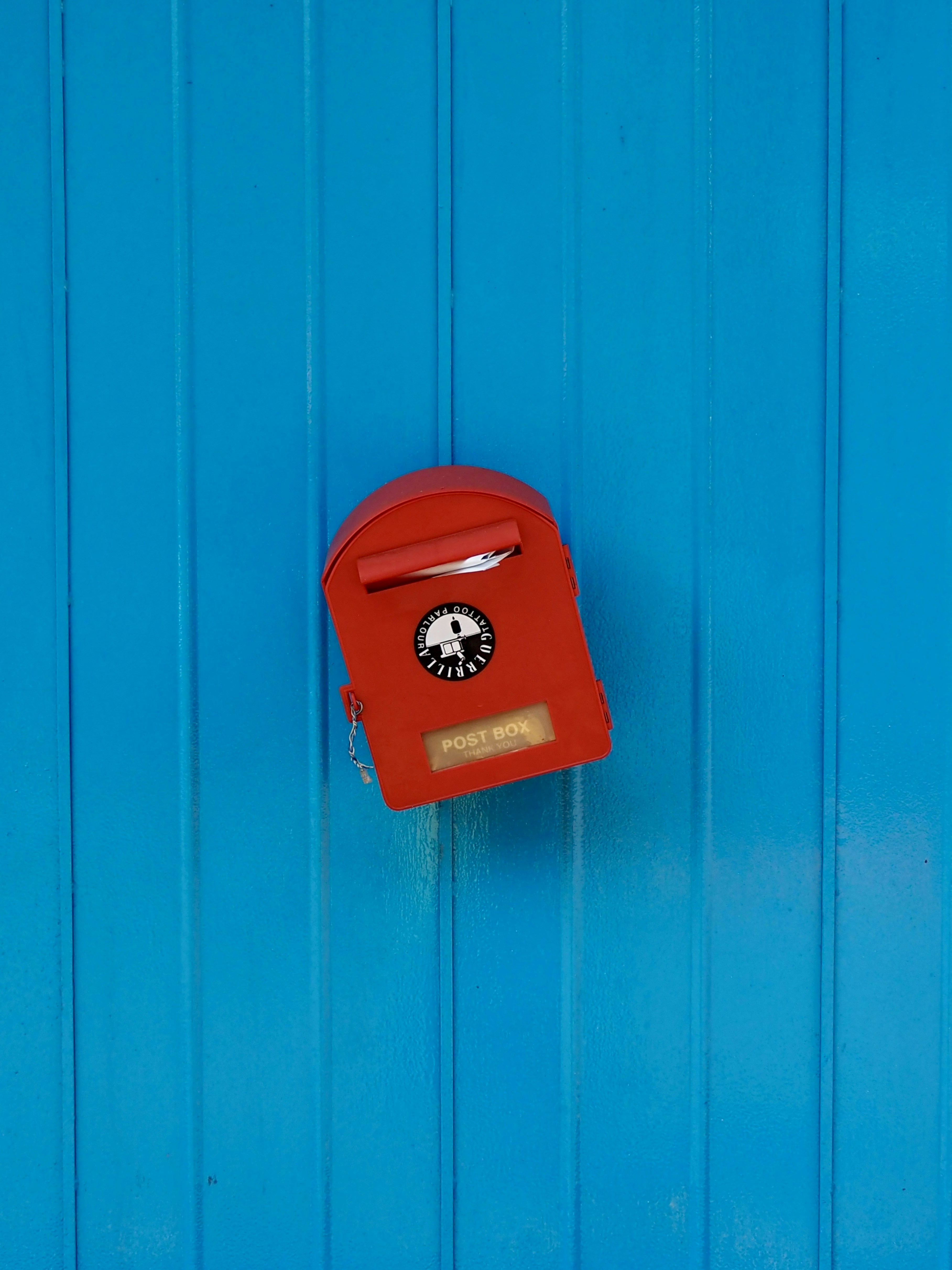 A bright red mailbox against a blue wooden wall