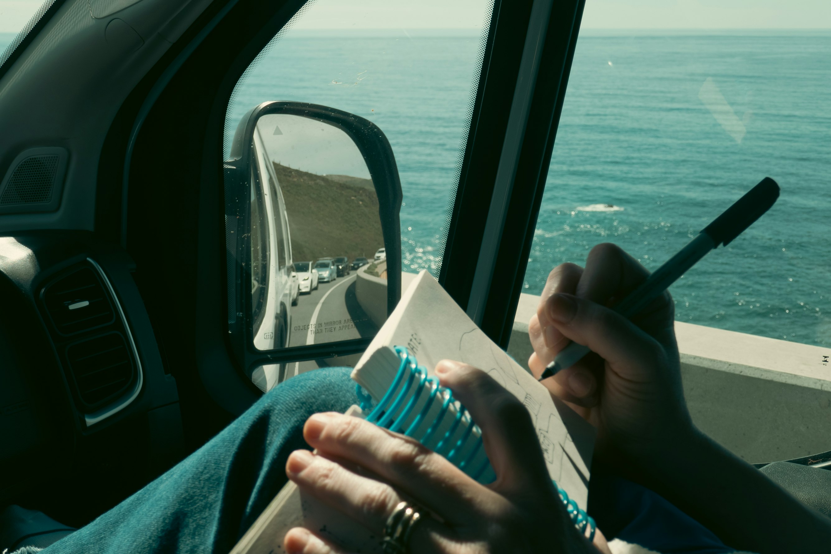 View of a coastal town with red-roofed buildings nestled against a steep green hillside by the sea