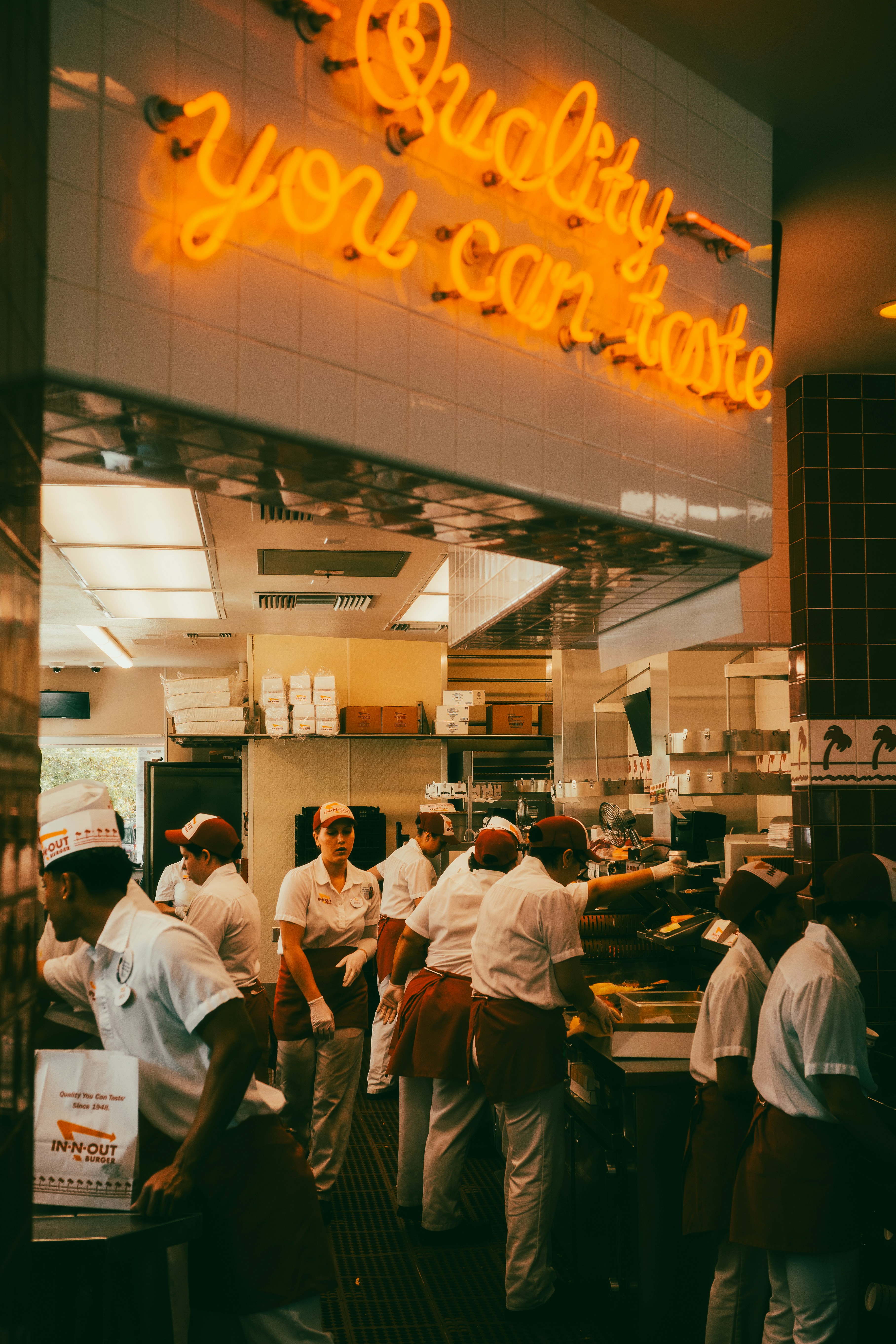 Mitarbeiter in einer belebten Fast-Food-Küche mit Neonschild.