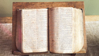 An open, aged book rests on a wooden stand.
